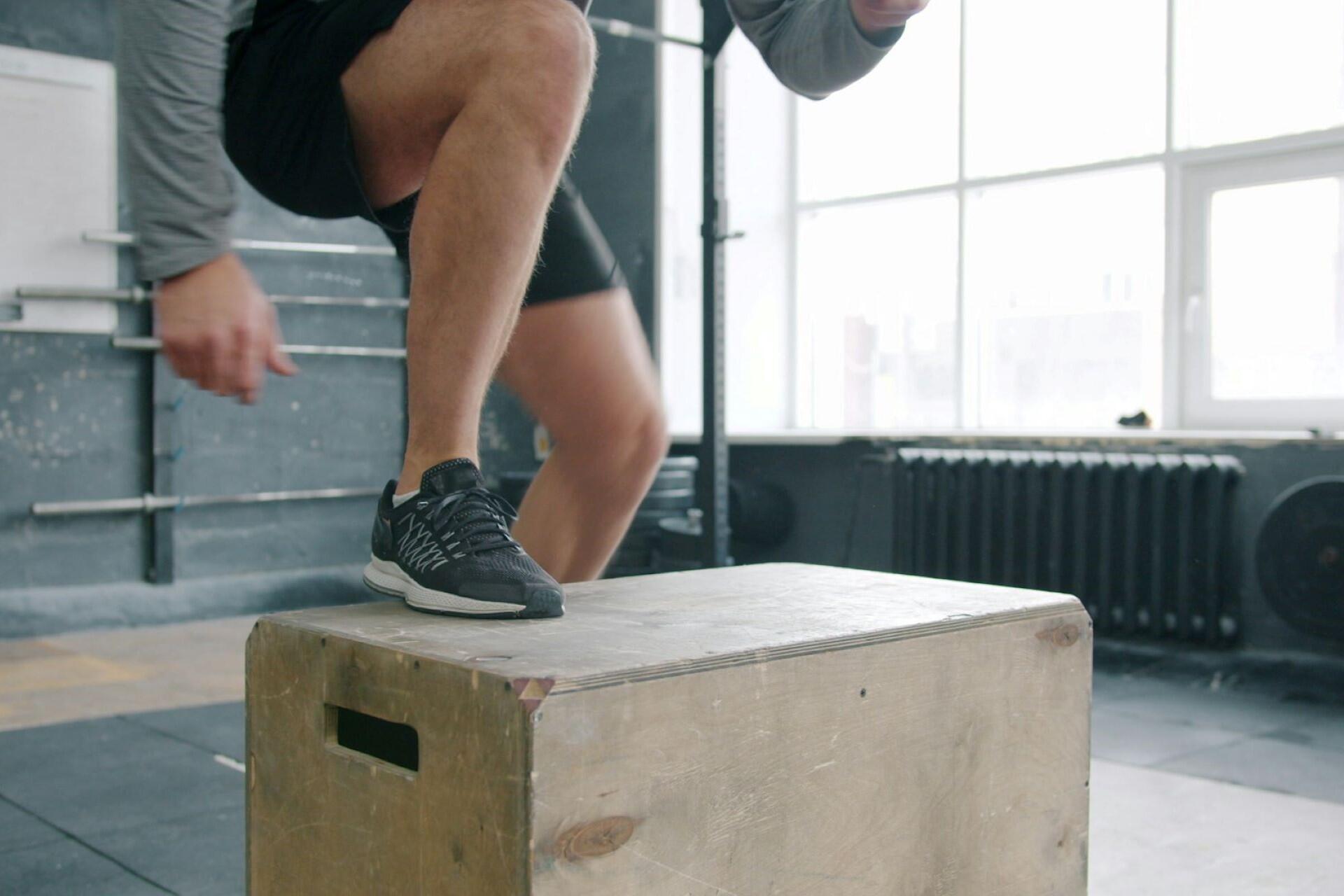 Athlete performing a plyometric box jump during a functional fitness workout in a gym