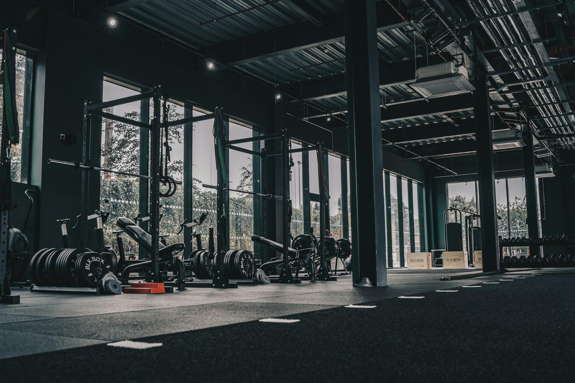 Modern functional fitness gym with squat racks, weight plates, rowing machines, and open training space.