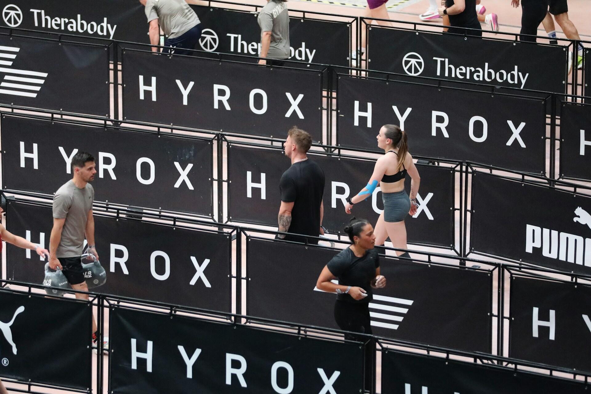 Athletes running through HYROX race lanes during a hybrid fitness competition