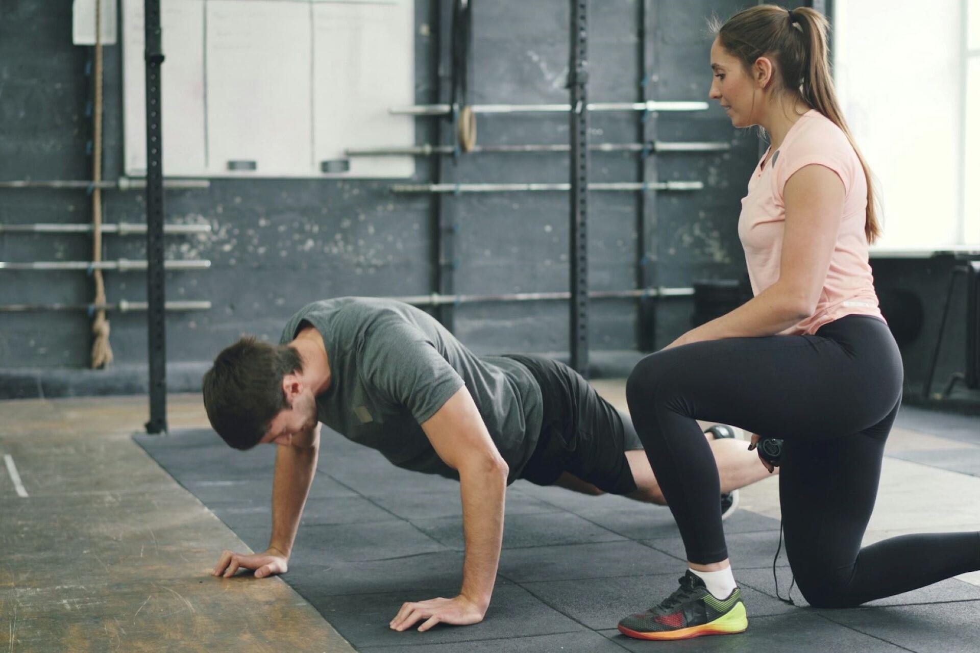 Personal trainer coaching an athlete doing push-ups during a strength workout in a gym