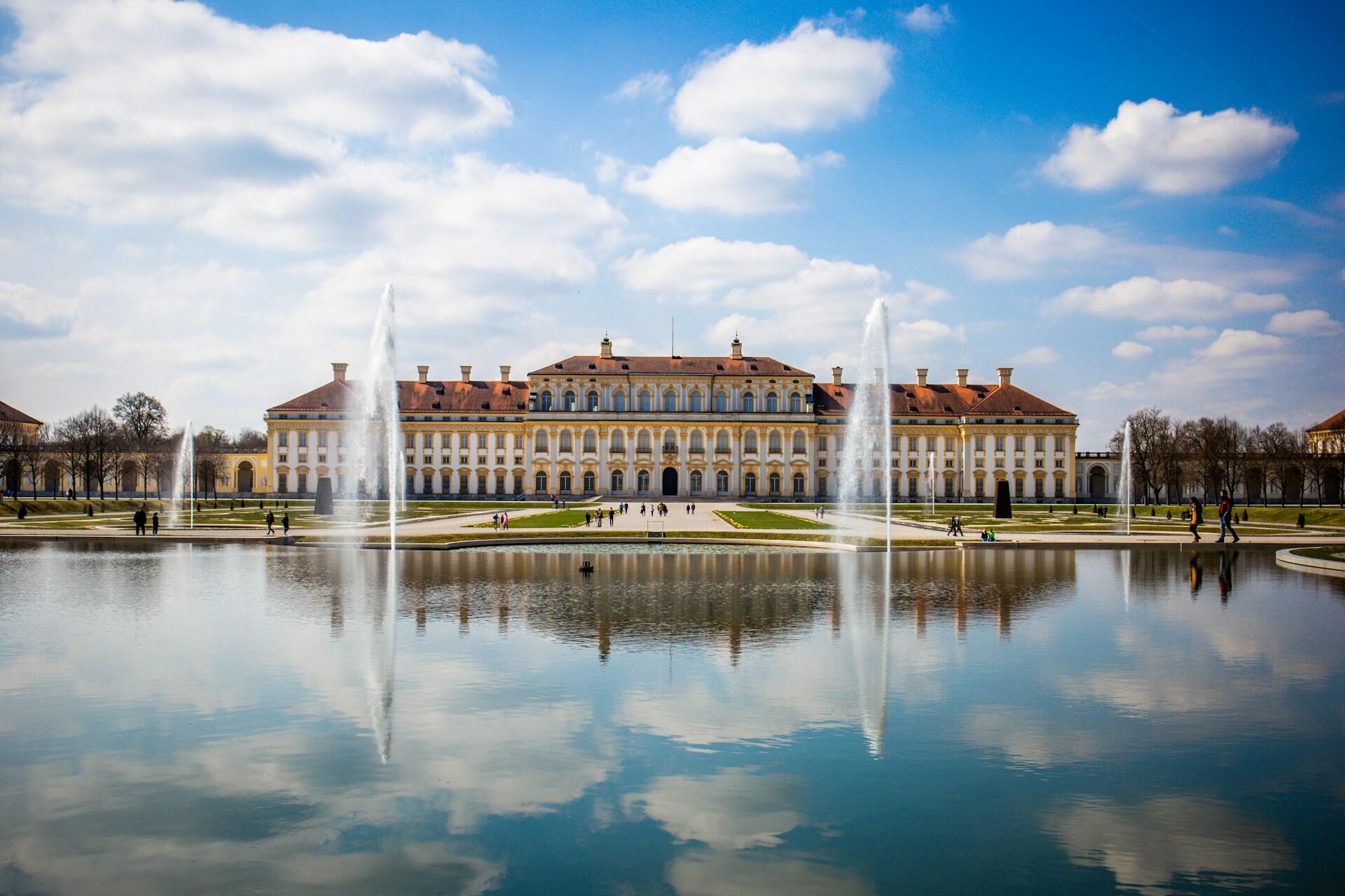 Schleißheim palace complex with fountains and reflecting pool under a partly cloudy sky, in Munich, Germany.