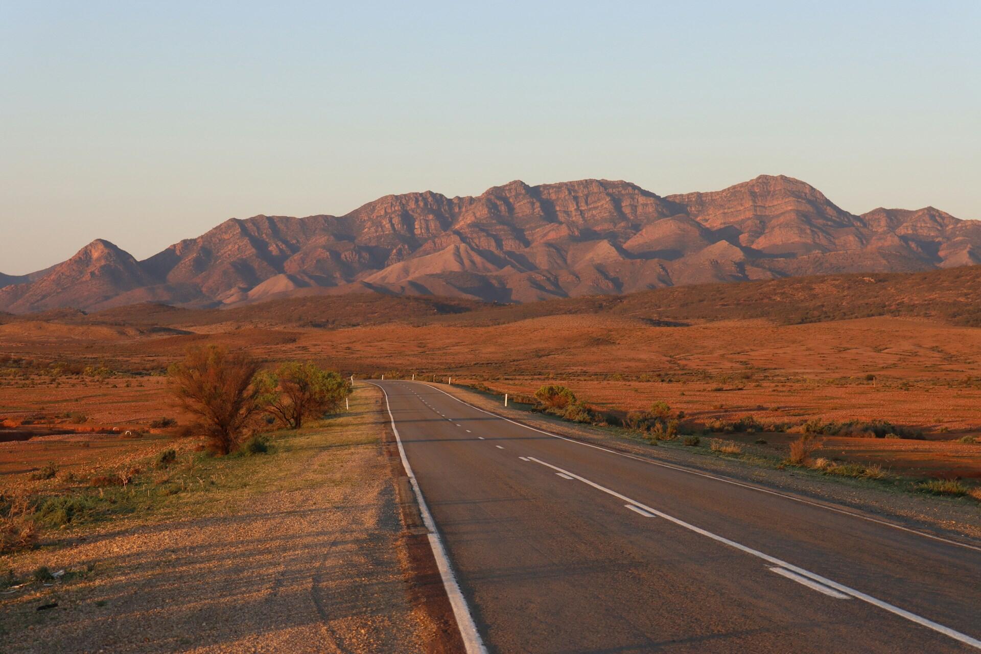 Long straight road through arid landscape with mountains in the distance