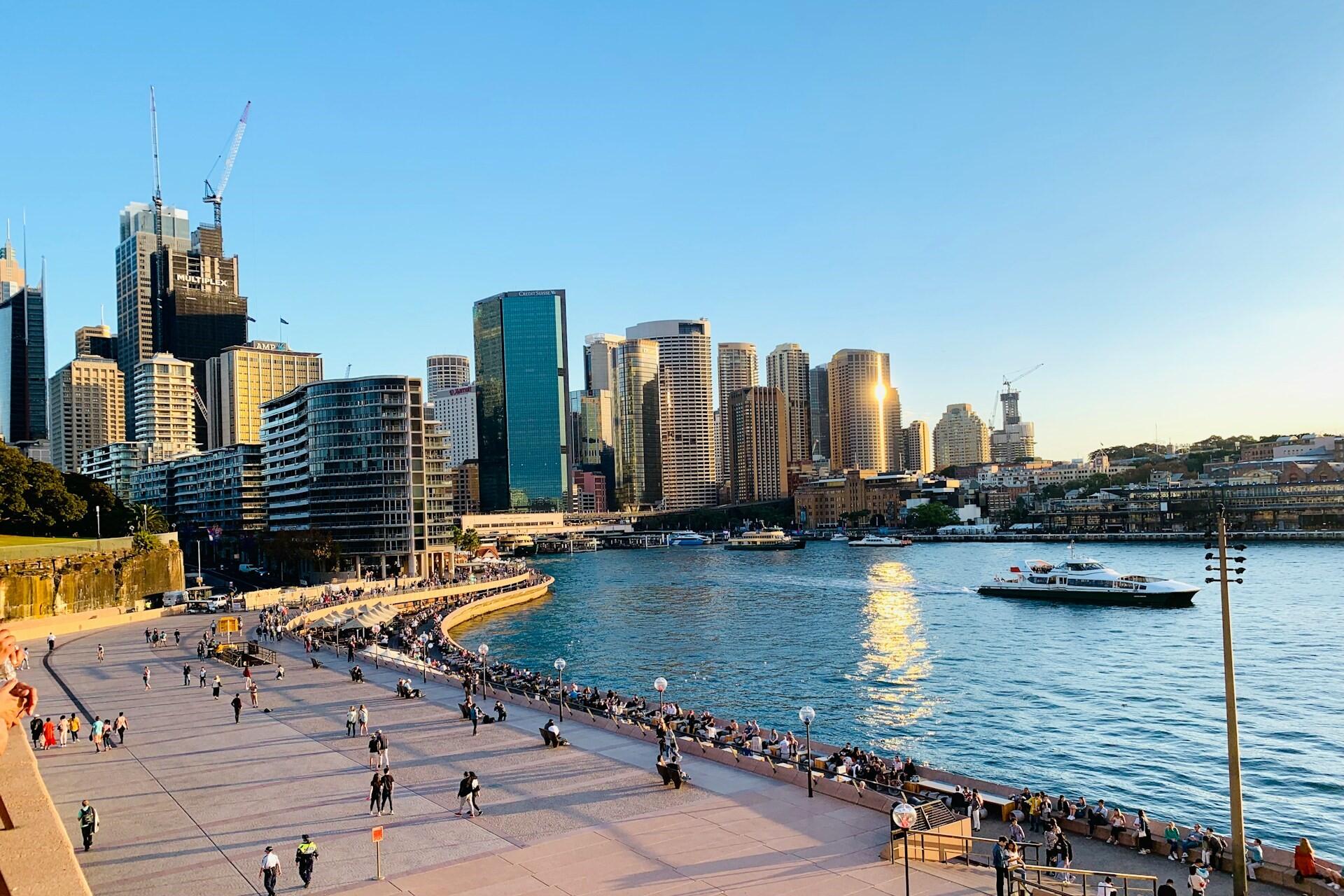 Sydney Harbour with city skyline, waterfront promenade, and boats on the water