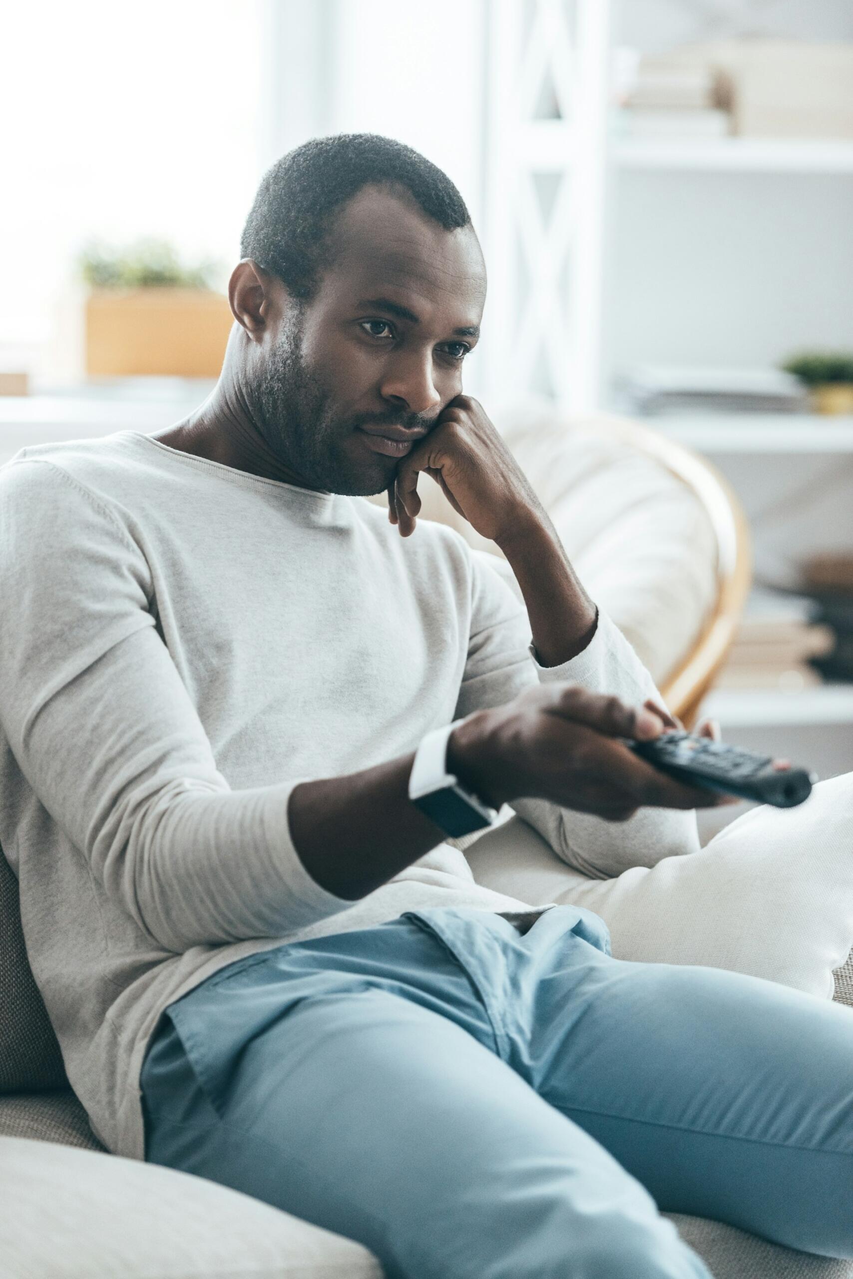 A man in a white shirt on a couch with a television remote in his hand. 