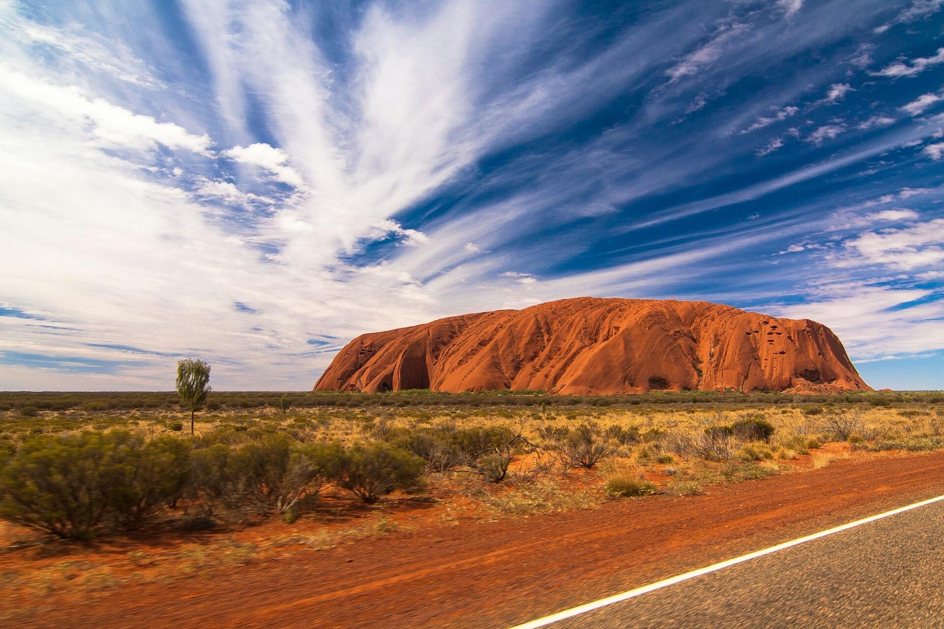 Uluru rock formation in the Australian outback surrounded by desert landscape and blue sky