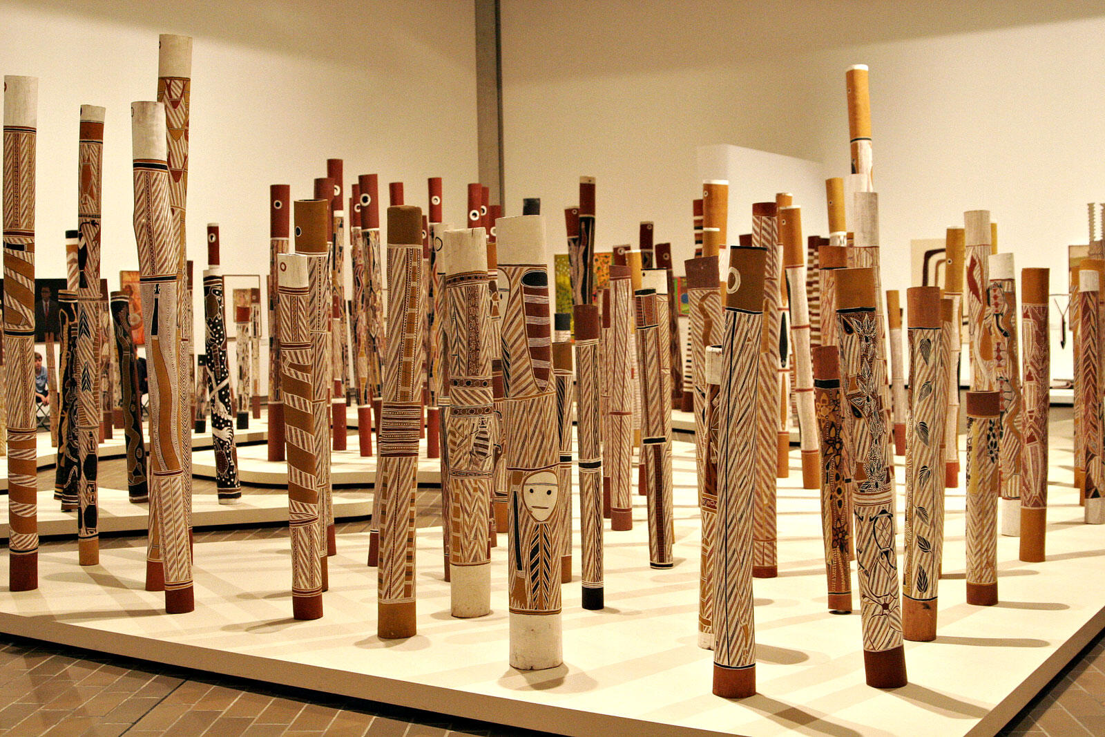 photo of art instillation at National Gallery Canberra of dozens of memorial poles: hollow sticks carved with patterns and motifs unique to each person