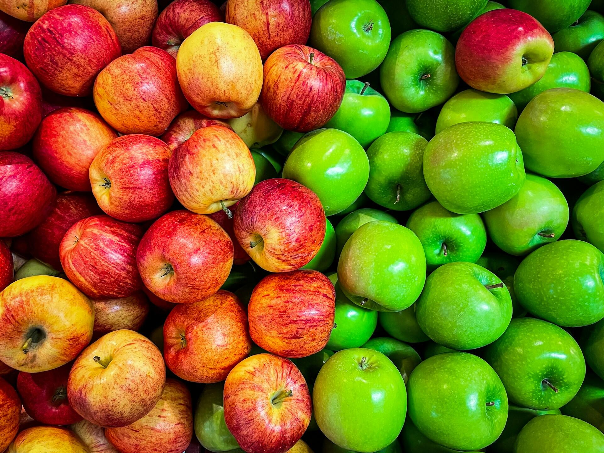 A pile of red and gold apples next to a pile of bright green apples. 