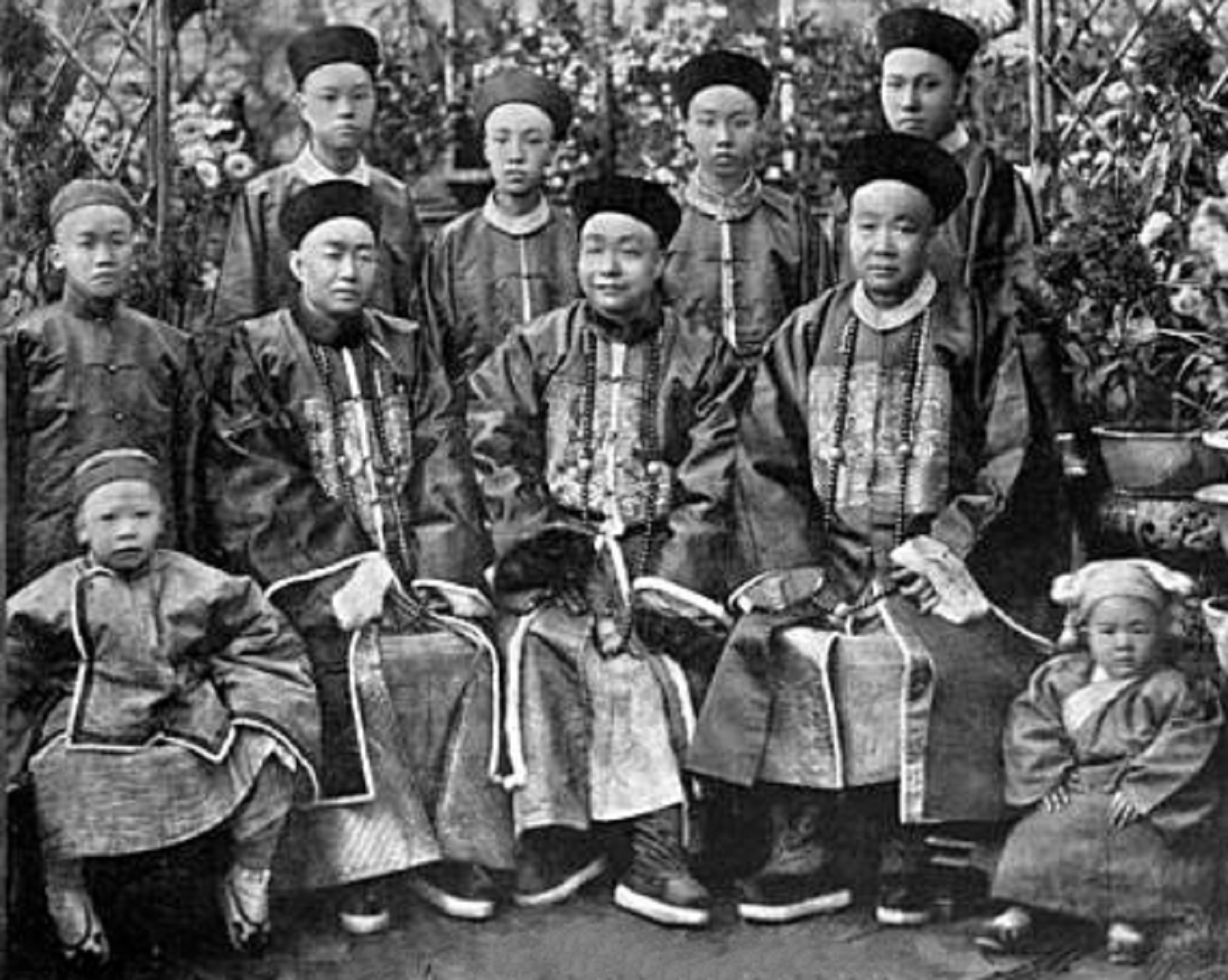 A richly-dressed Chinese family, featuring only males, poses three-deep for a portrait.