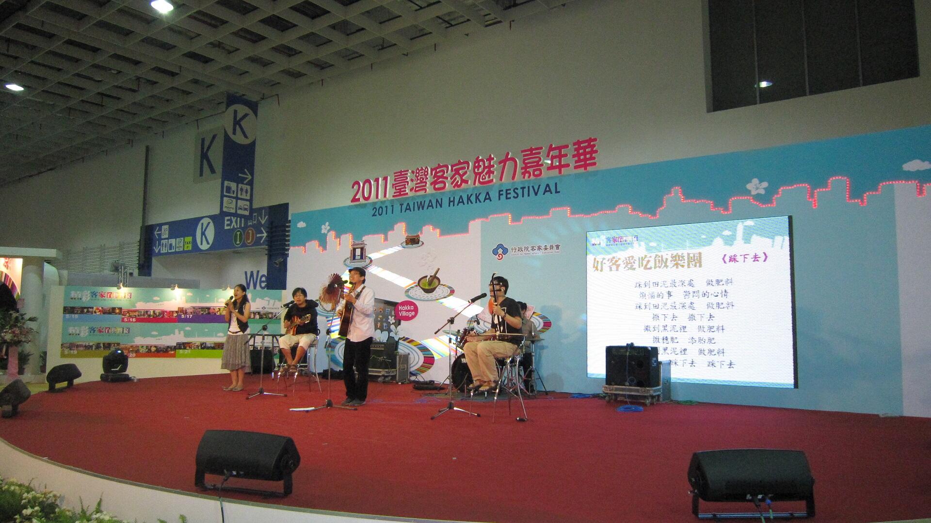 Musicians on a vast stage with a red floor, in front of a blue backdrop with Chinese and English writing.