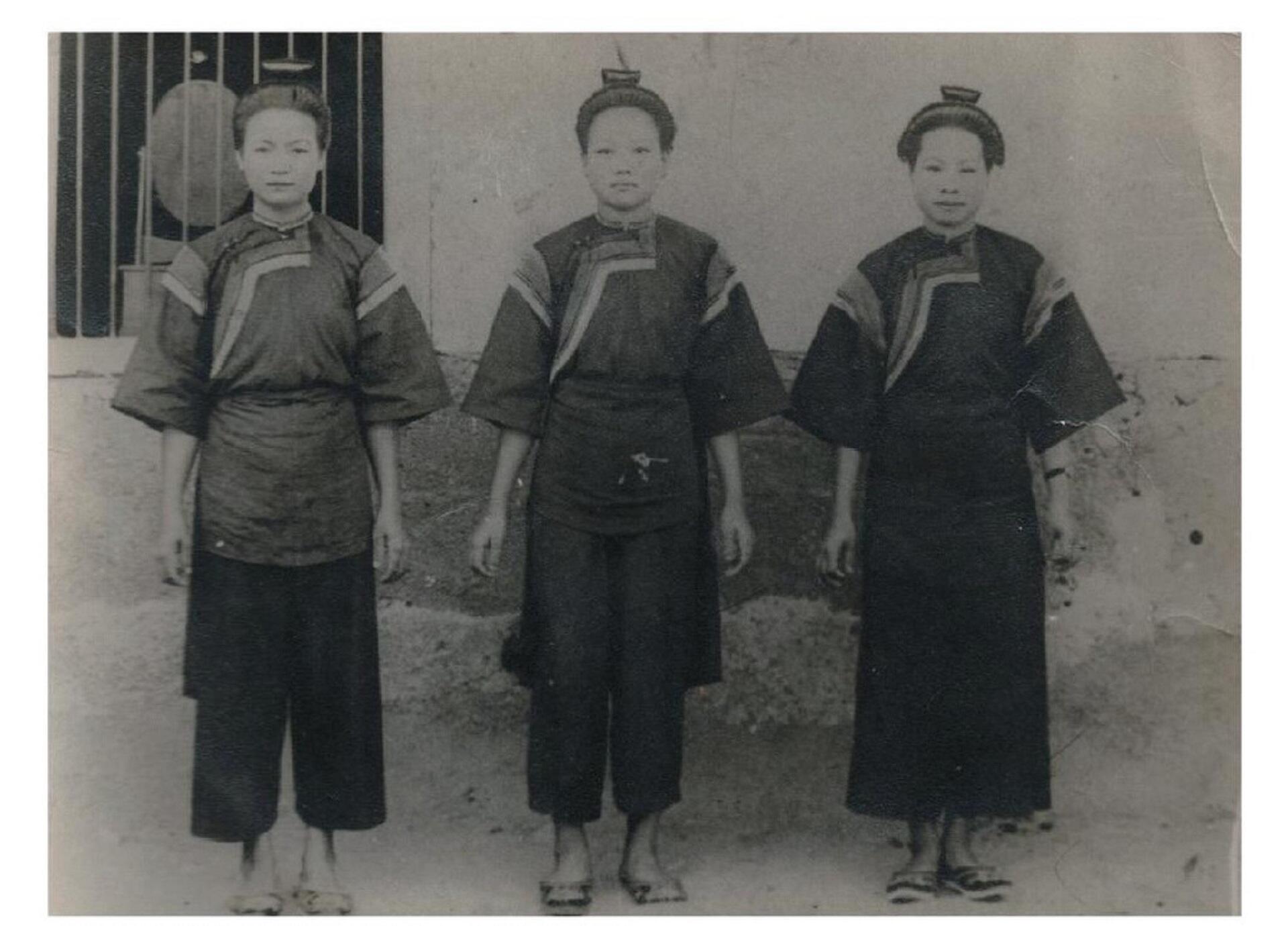 Three women with their hair in a topknot, wearing practical clothing, standing in front of a plain wall.
