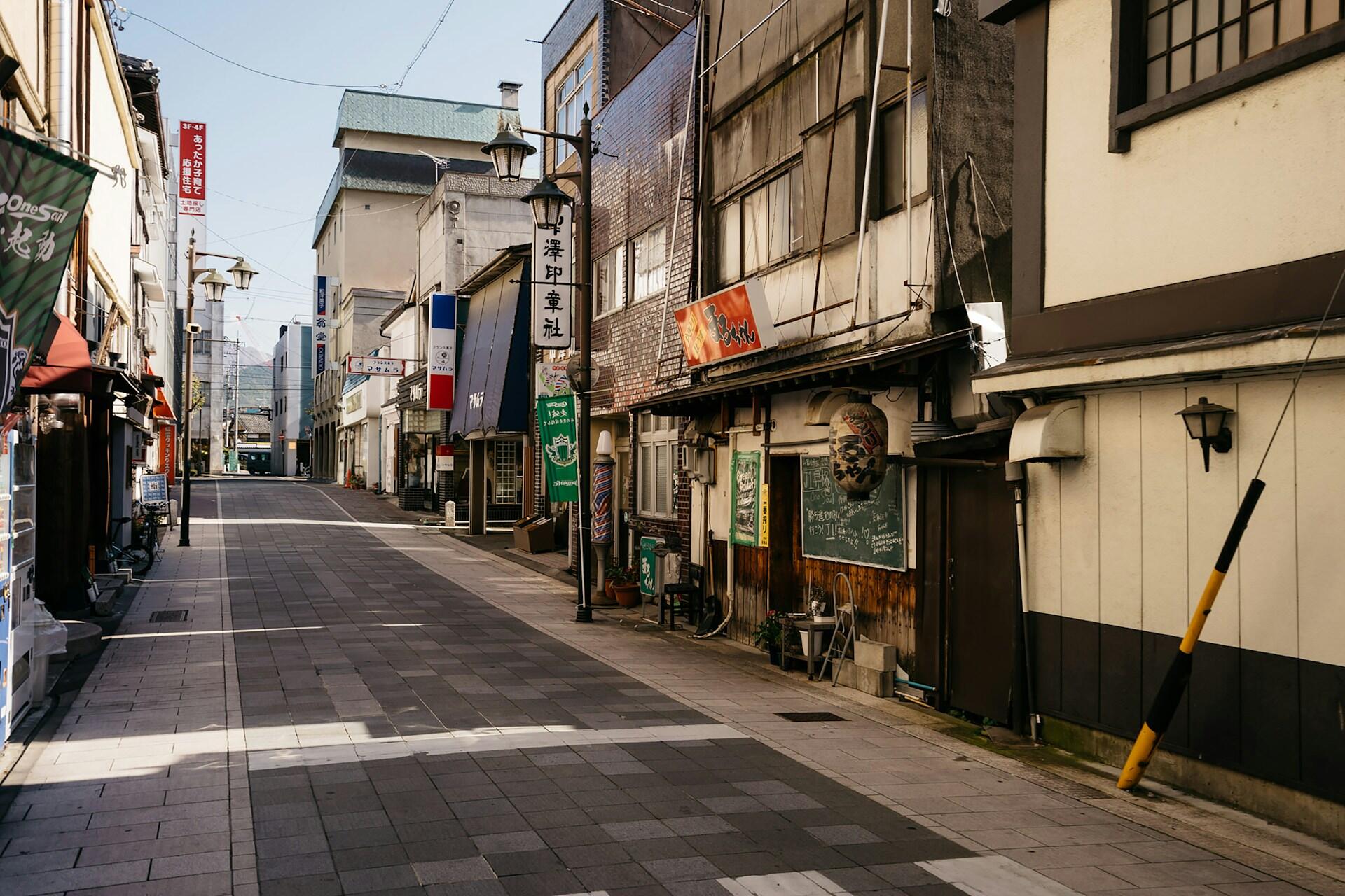 A narrow, empty street on a sunny day, with shops lining the way. The atmosphere is tranquil and the street is very clean.