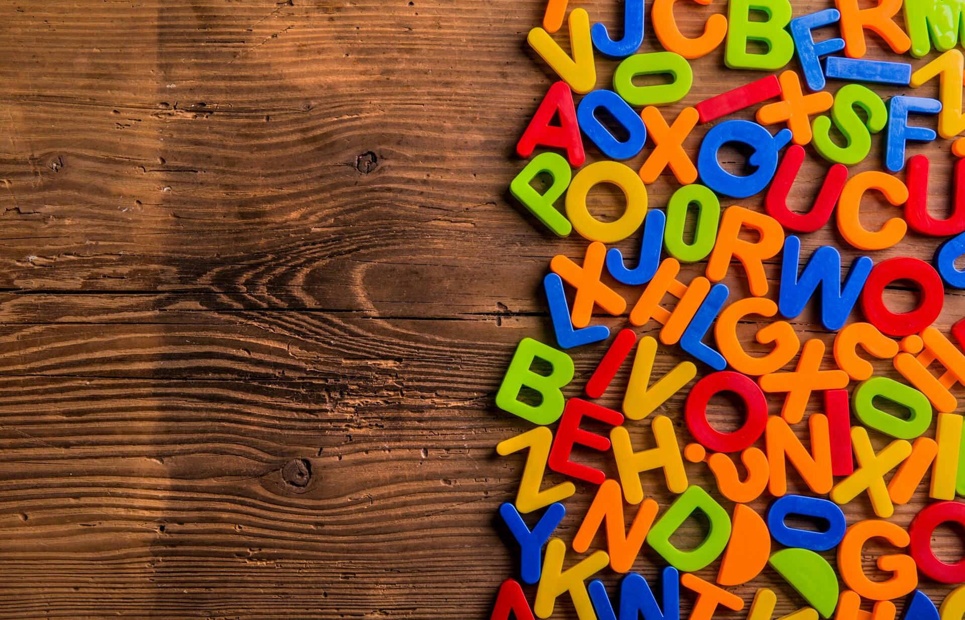 Colorful plastic alphabet letters scattered on the right side of a wooden surface.