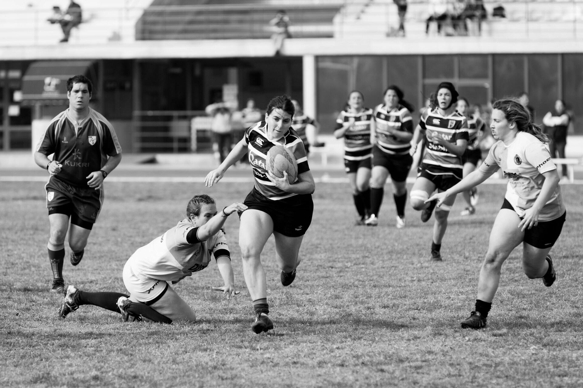Black-and-white photo of women playing rugby on a grass field