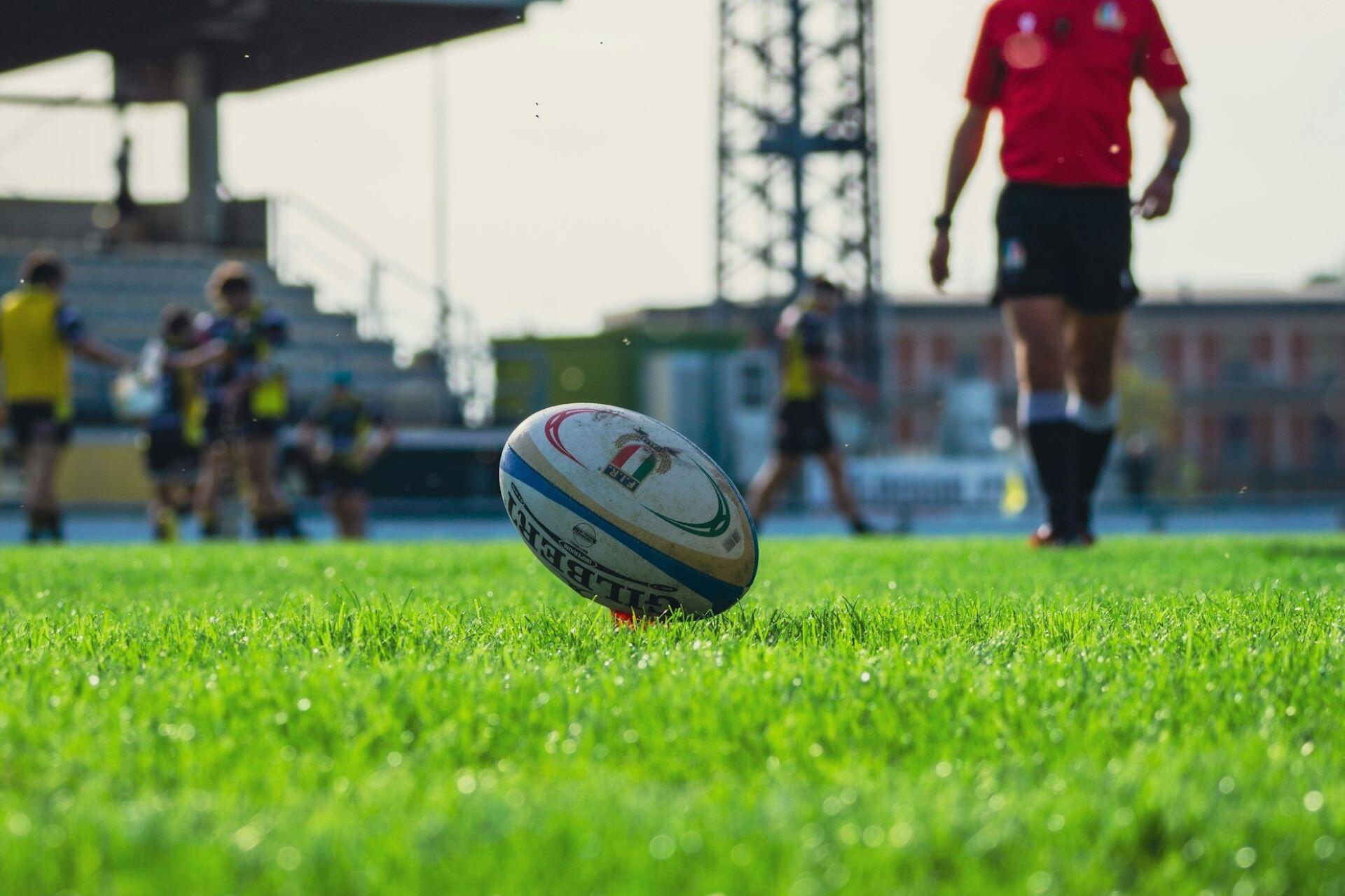 Rugby ball on grass with players and a referee blurred in the background