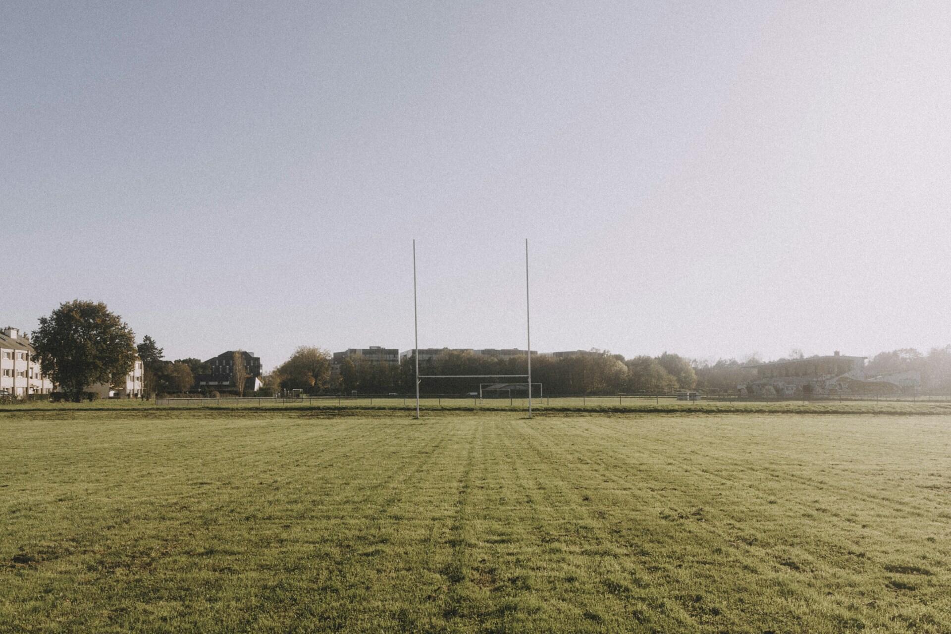 Rugby posts on a grassy field with buildings and trees in the background