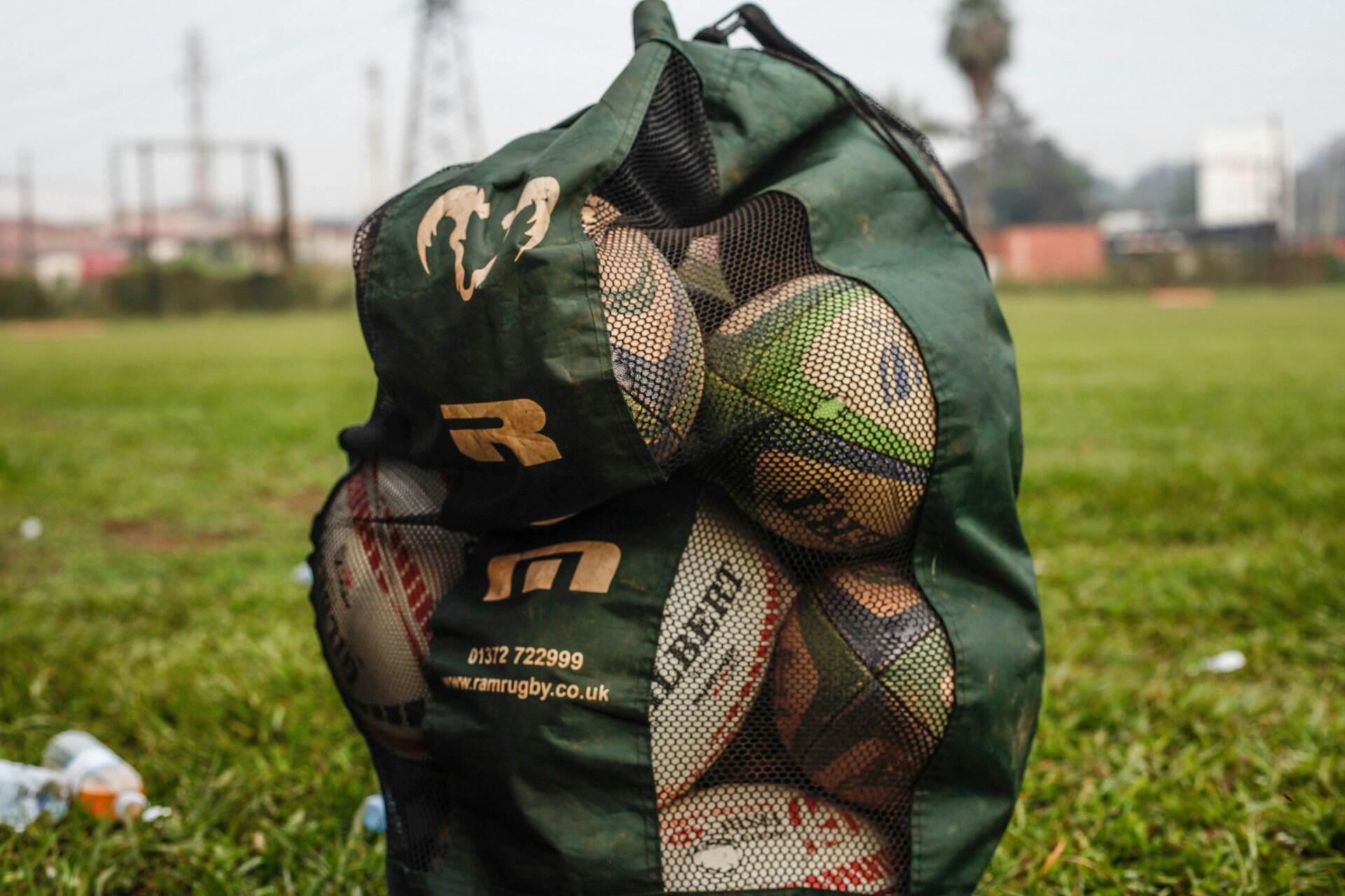 Rugby balls in a green mesh equipment bag on grass