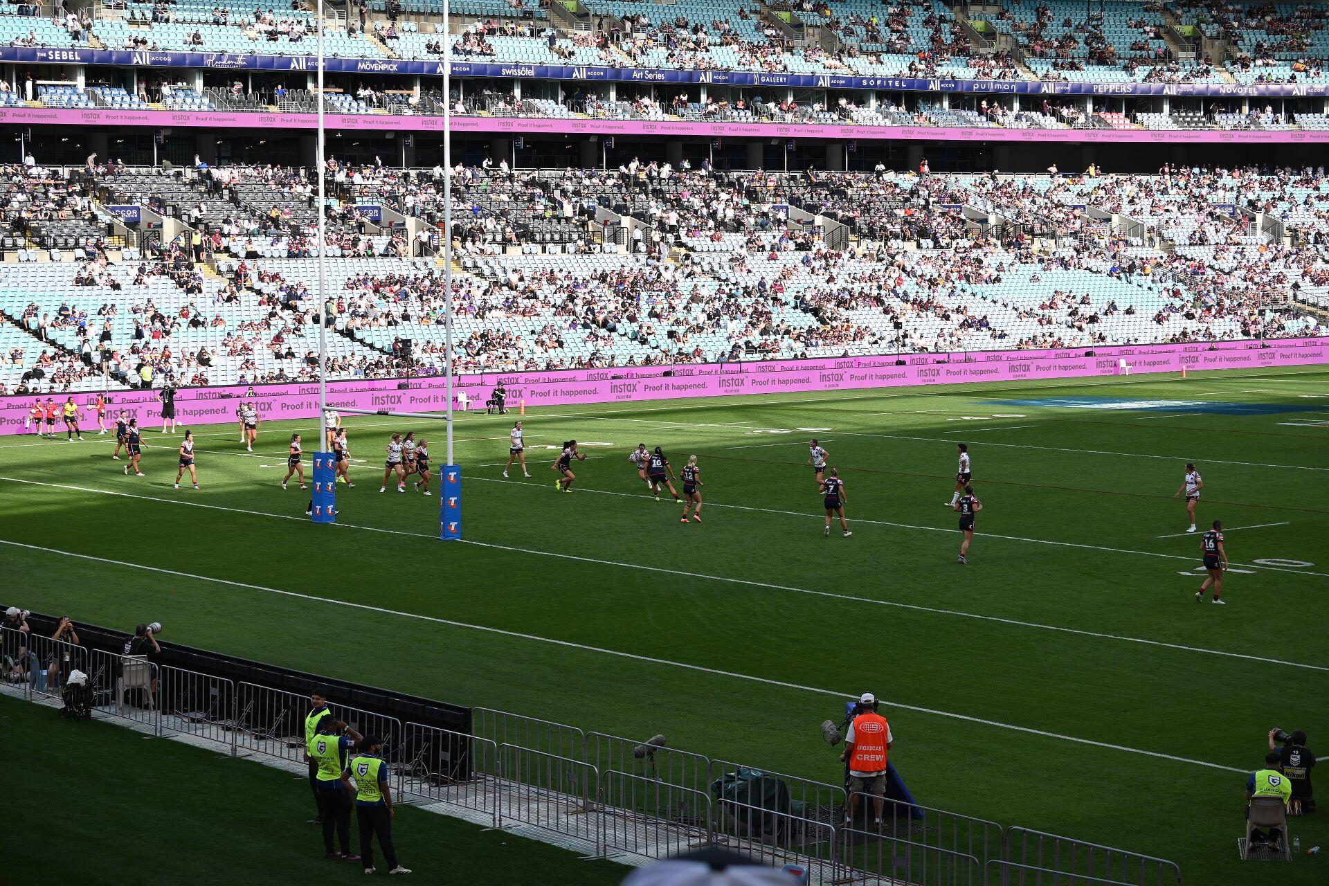 Rugby league players on a field in a large stadium with spectators in the stands