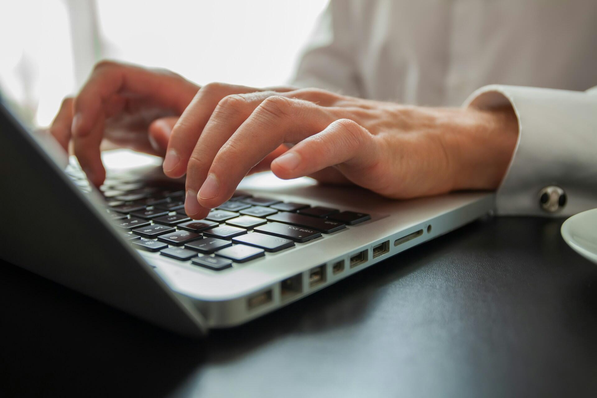 A person typing on a silver laptop's keyboard.