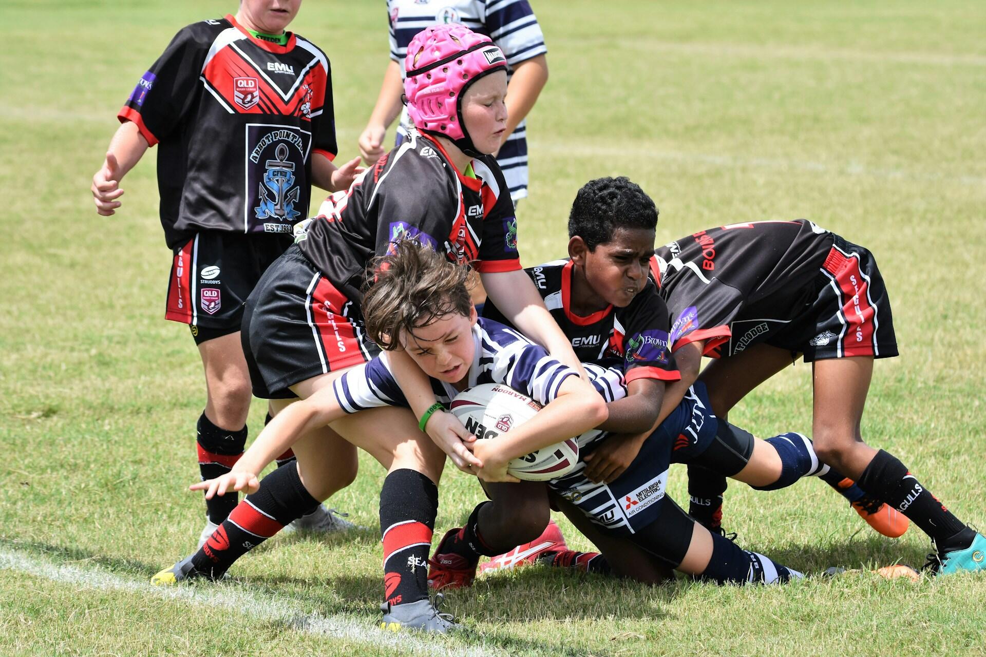 Young rugby players tackling a ball carrier on a grass field