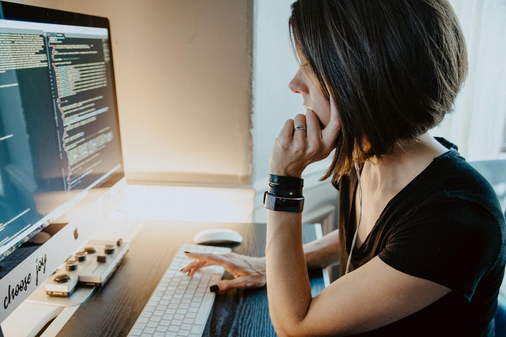 A woman with short brown hair sits in front of a large computer screen looking pensively at the information displayed there.