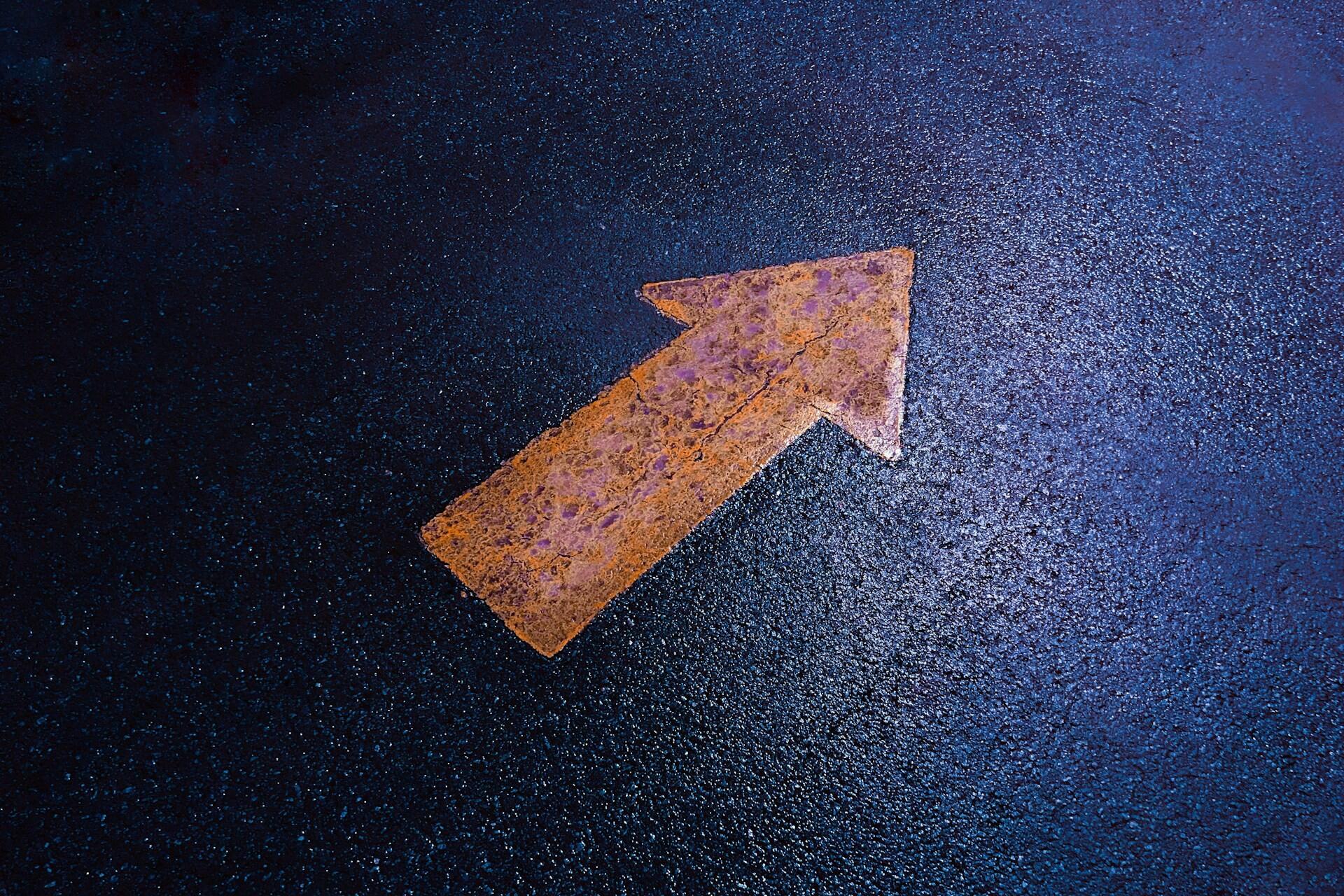 Orange arrow painted on dark wet road