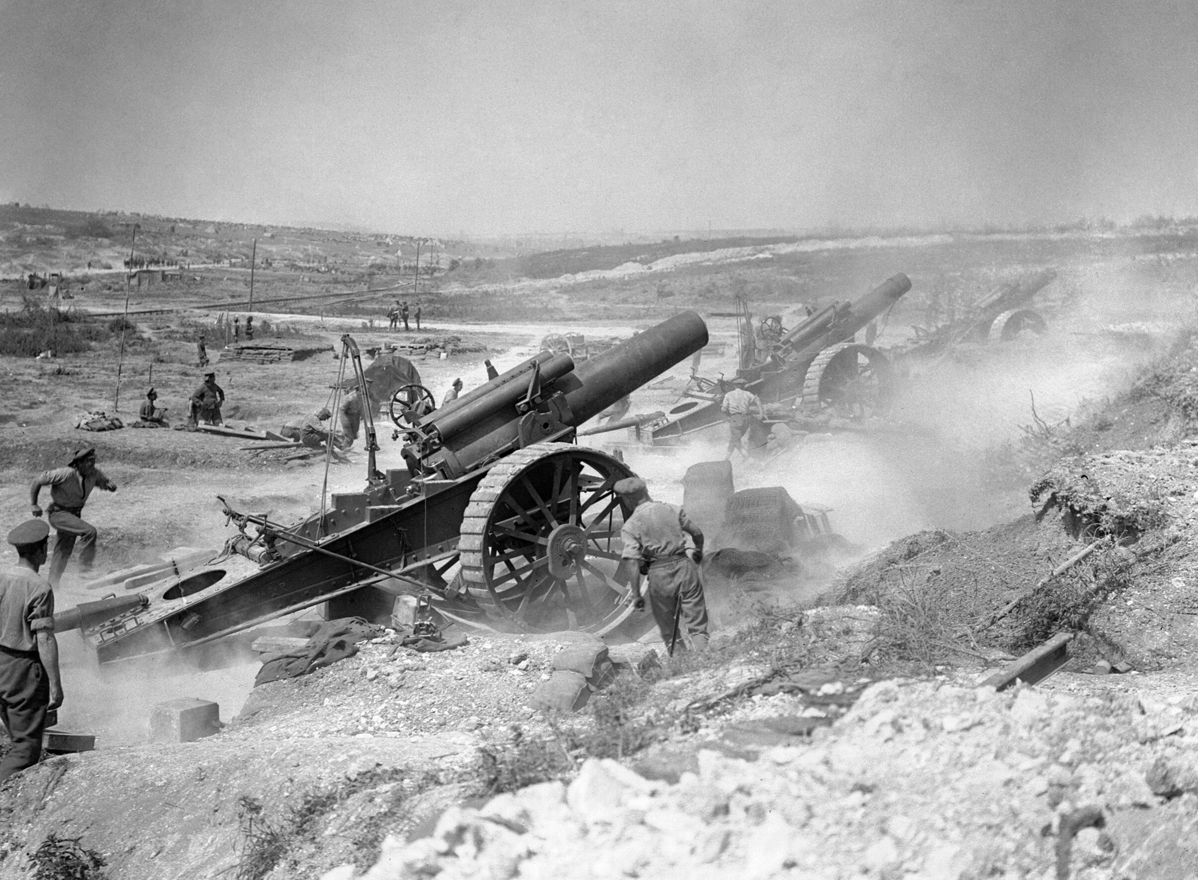 Black-and-white photograph of British soldiers operating large howitzers amid clouds of smoke during the Battle of the Somme in France, 1916.