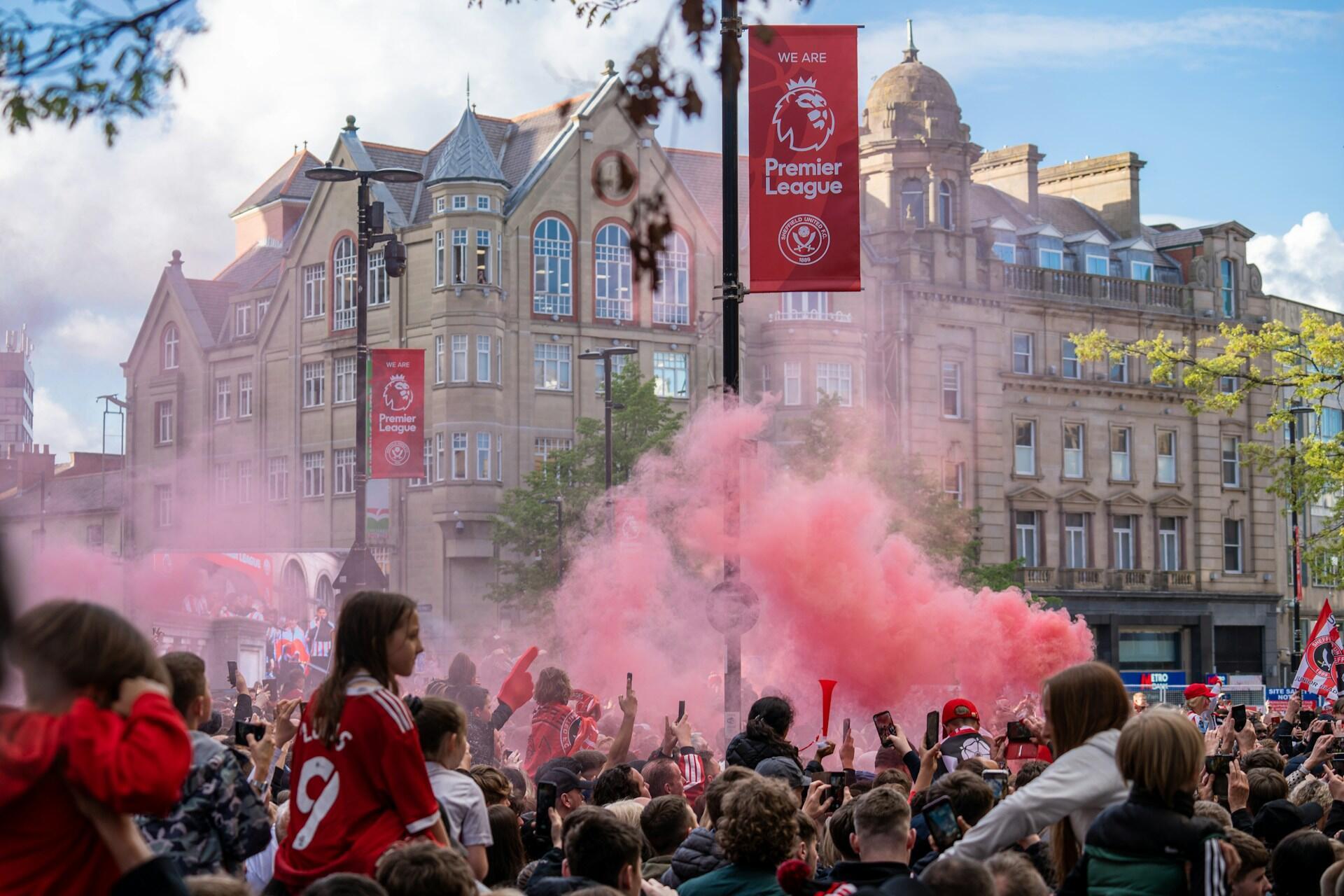 A lively crowd at a Premier League game, with red smoke creating a festive atmosphere.