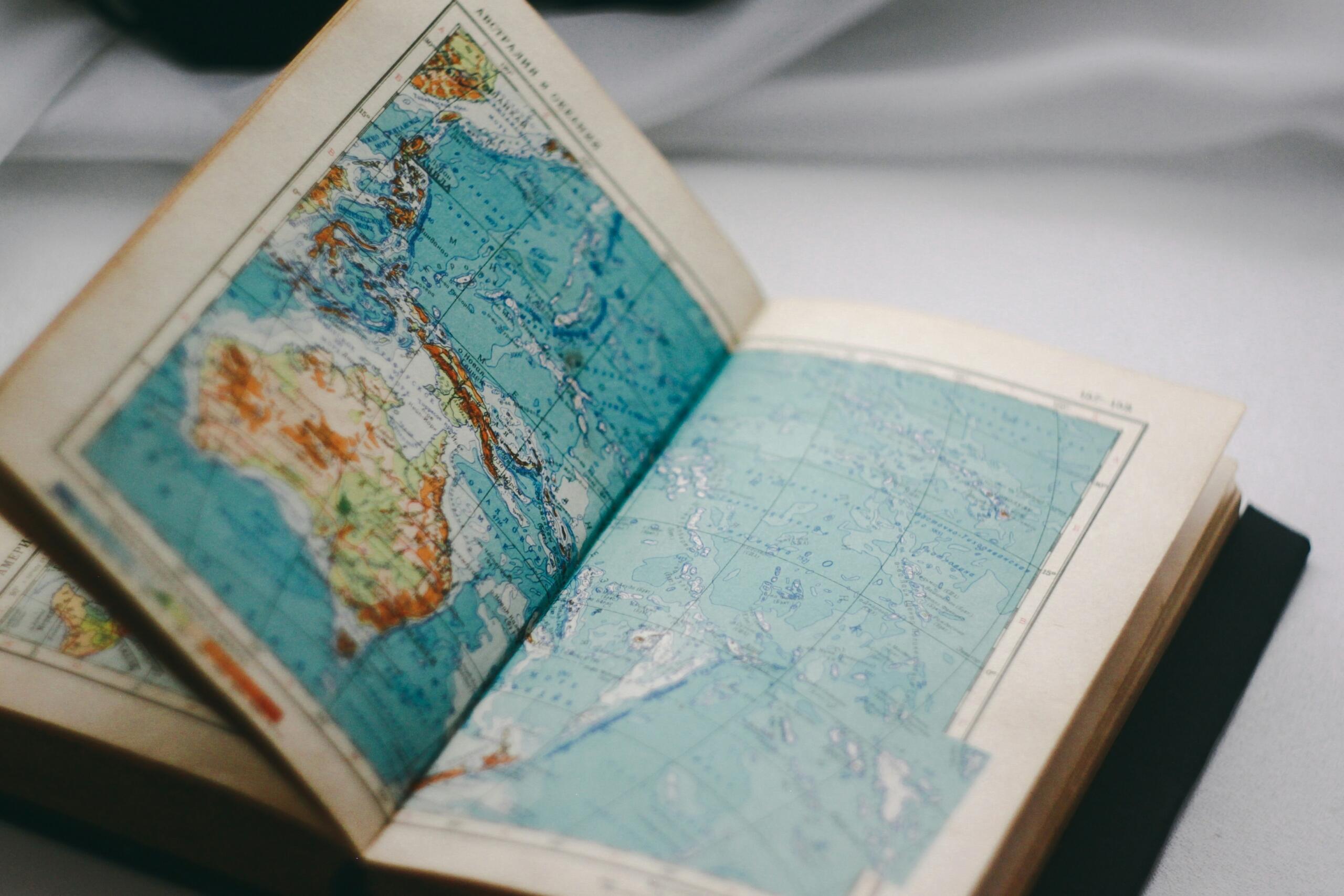 Otvoreni stari atlas s detaljnim kartama svijeta, vizuelna metafora za učenje geografskih pojmova i definicija.