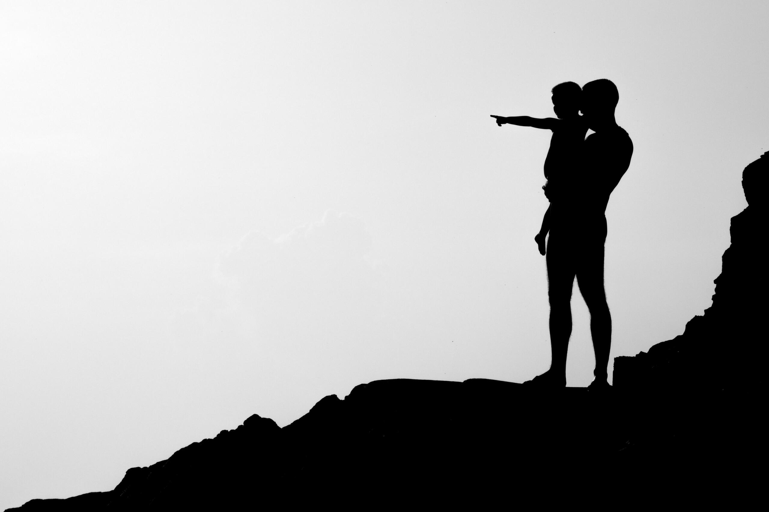 crno-bijela slika roditelja koji drži dijete s pogledom na vrh brda