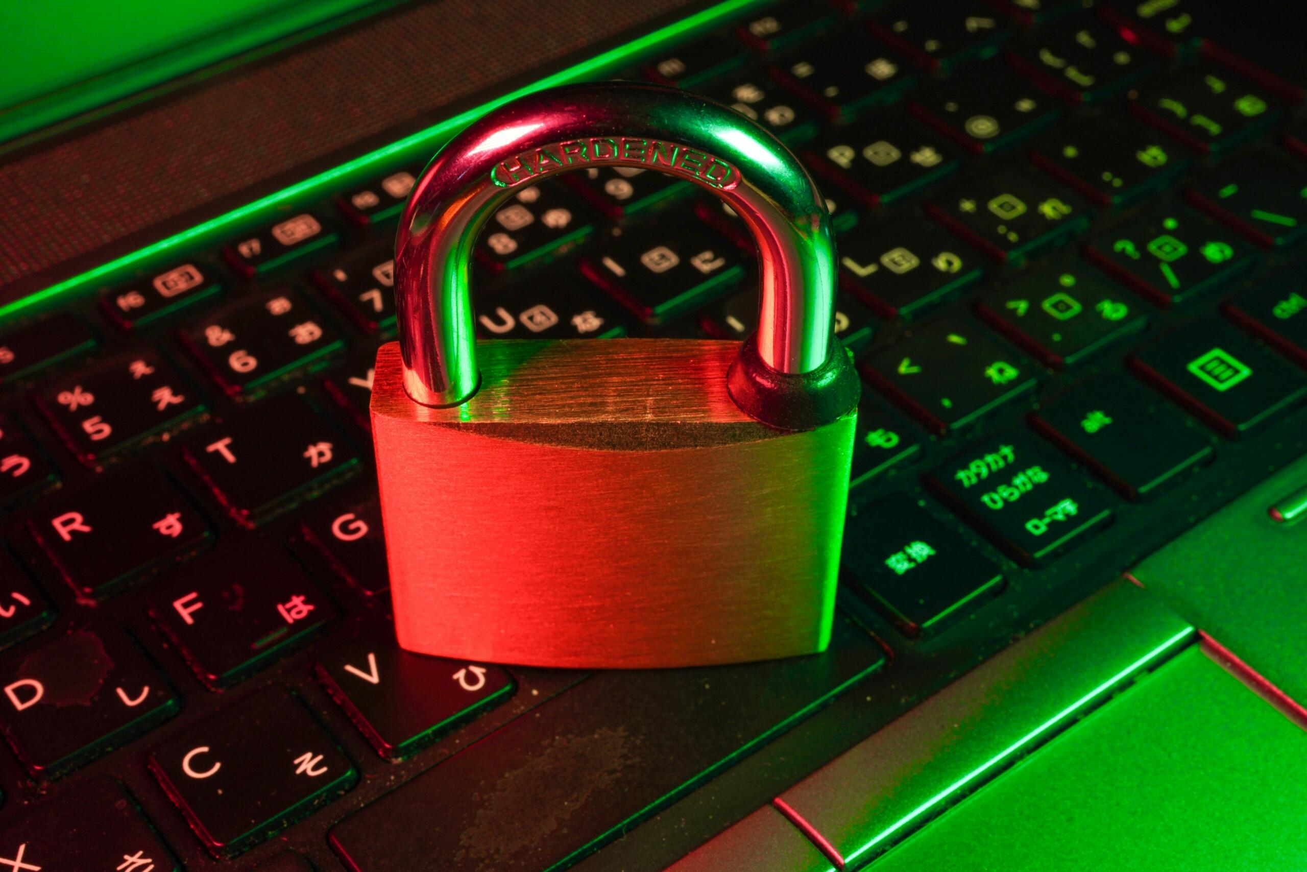 Objašnjenje kibernetičkih napada – krupni kadar metalnog katanca na tastaturi laptopa osvijetljenog crvenim i zelenim neonskim svjetlom kao simbol sajber sigurnosti.