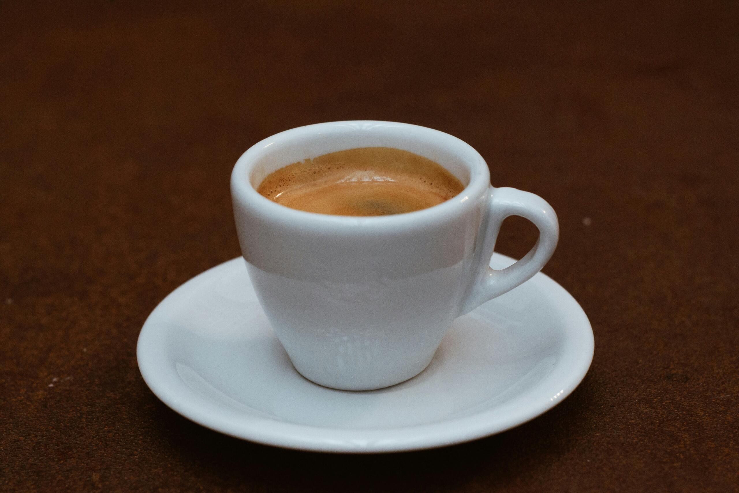 Austrijski njemački jezik – bijela porculanska šoljica sa svježe pripremljenom espresso kafom i finom kremom na bijelom tanjuriću.