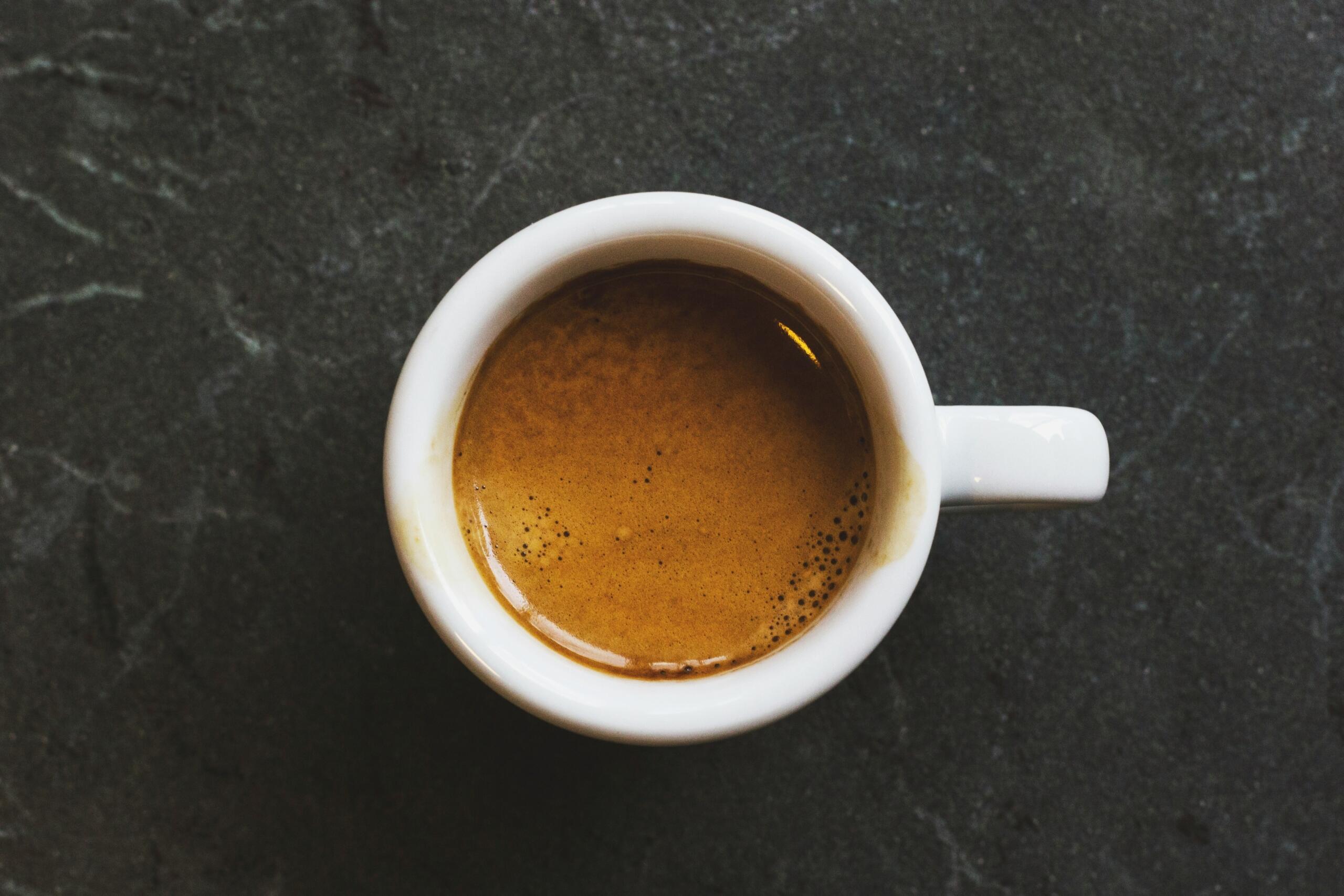 Netačan izgovor na engleskom jeziku – pogled odozgo na malu bijelu šoljicu svježe skuhanog espresso napitka sa gustom kremom, postavljenu na tamnu kamenu podlogu.
