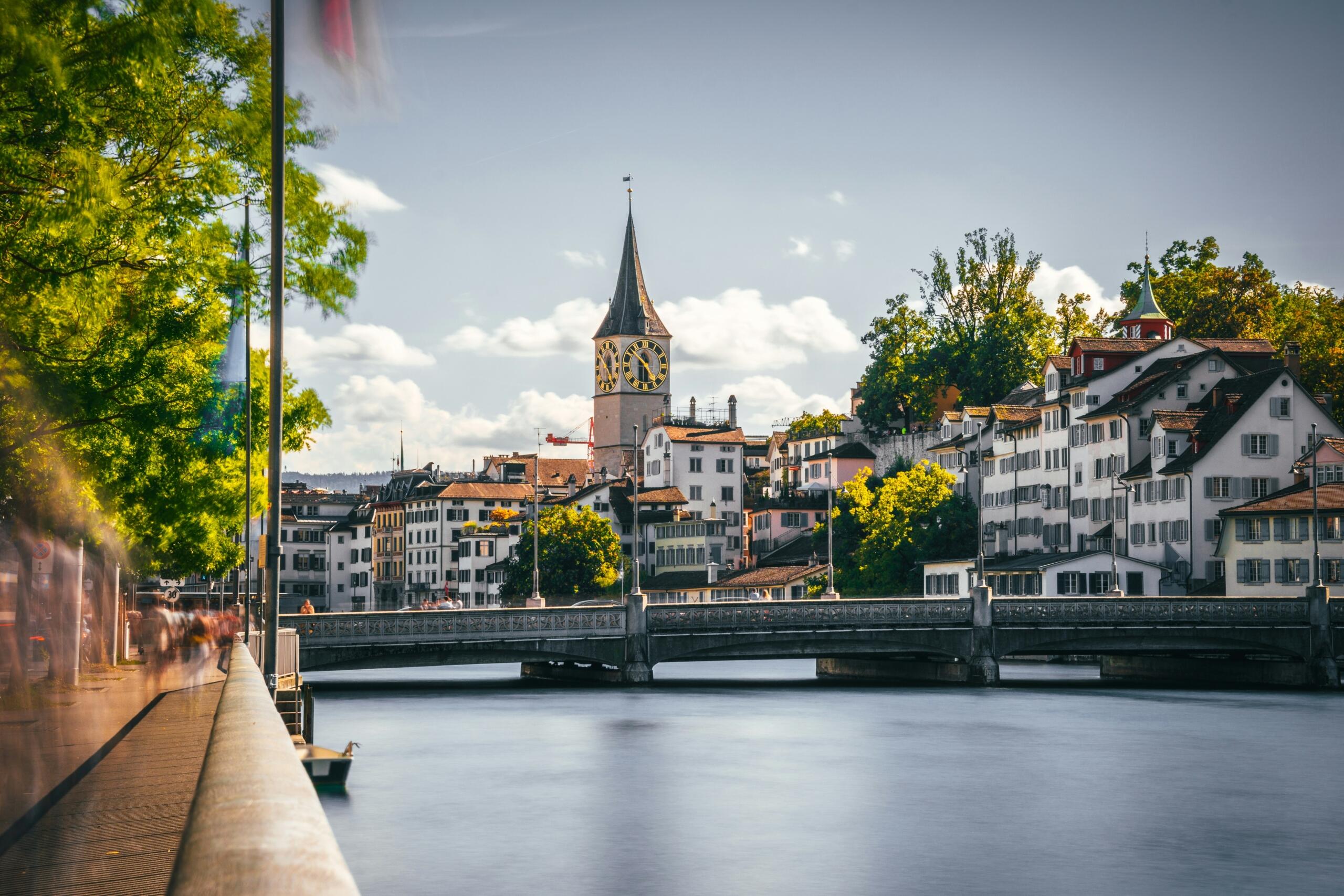 Švicarski njemački dijalekti – panorama grada Ciriha sa rijekom Limmat, historijskim tornjevima crkava i mostovima pod vedrim nebom.