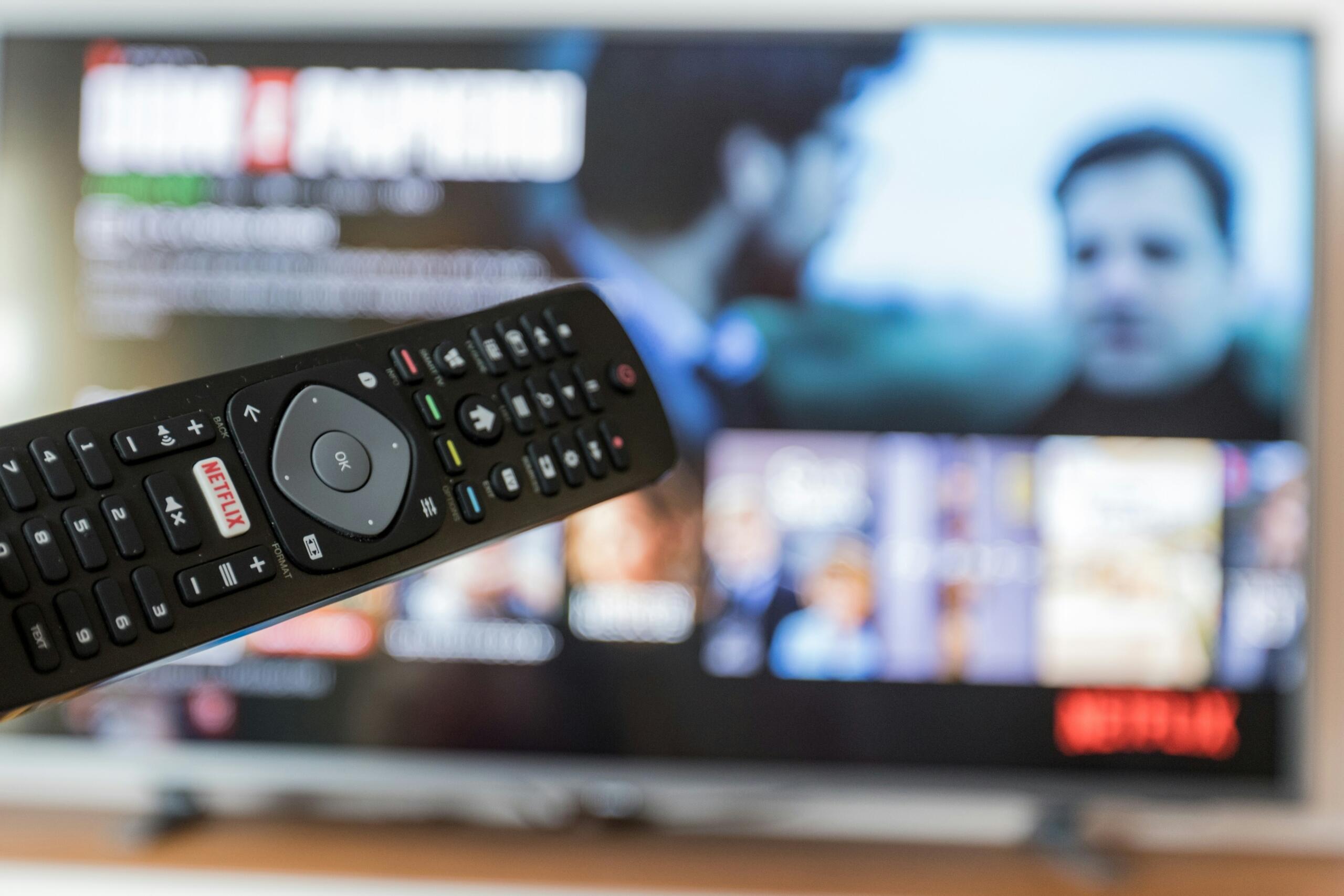 Daljinski upravljač u prvom planu okrenut prema televizoru na kojem je pokrenuta striming aplikacija