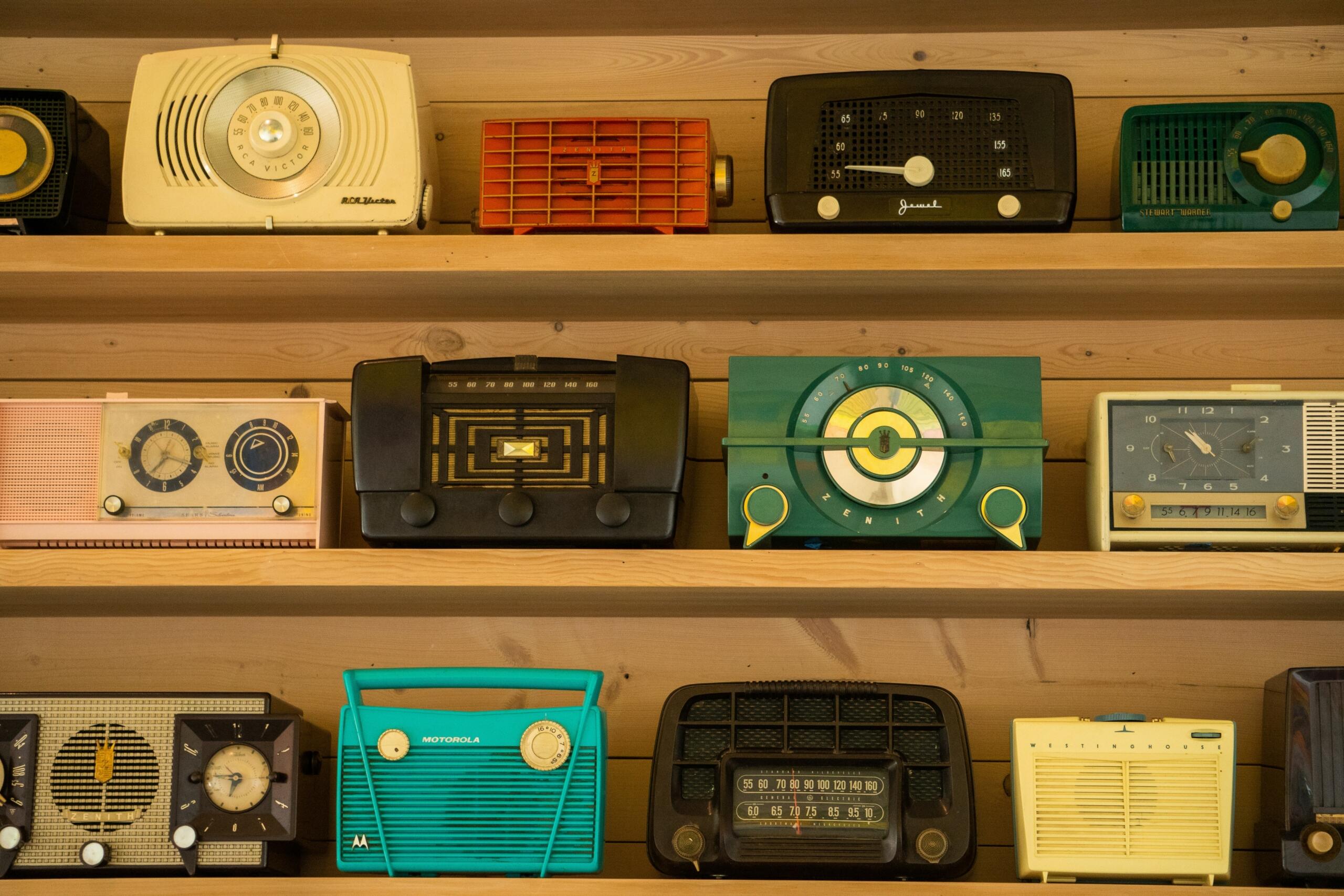 Kolekcija raznobojnih vintage radio aparata poredanih na drvenim policama