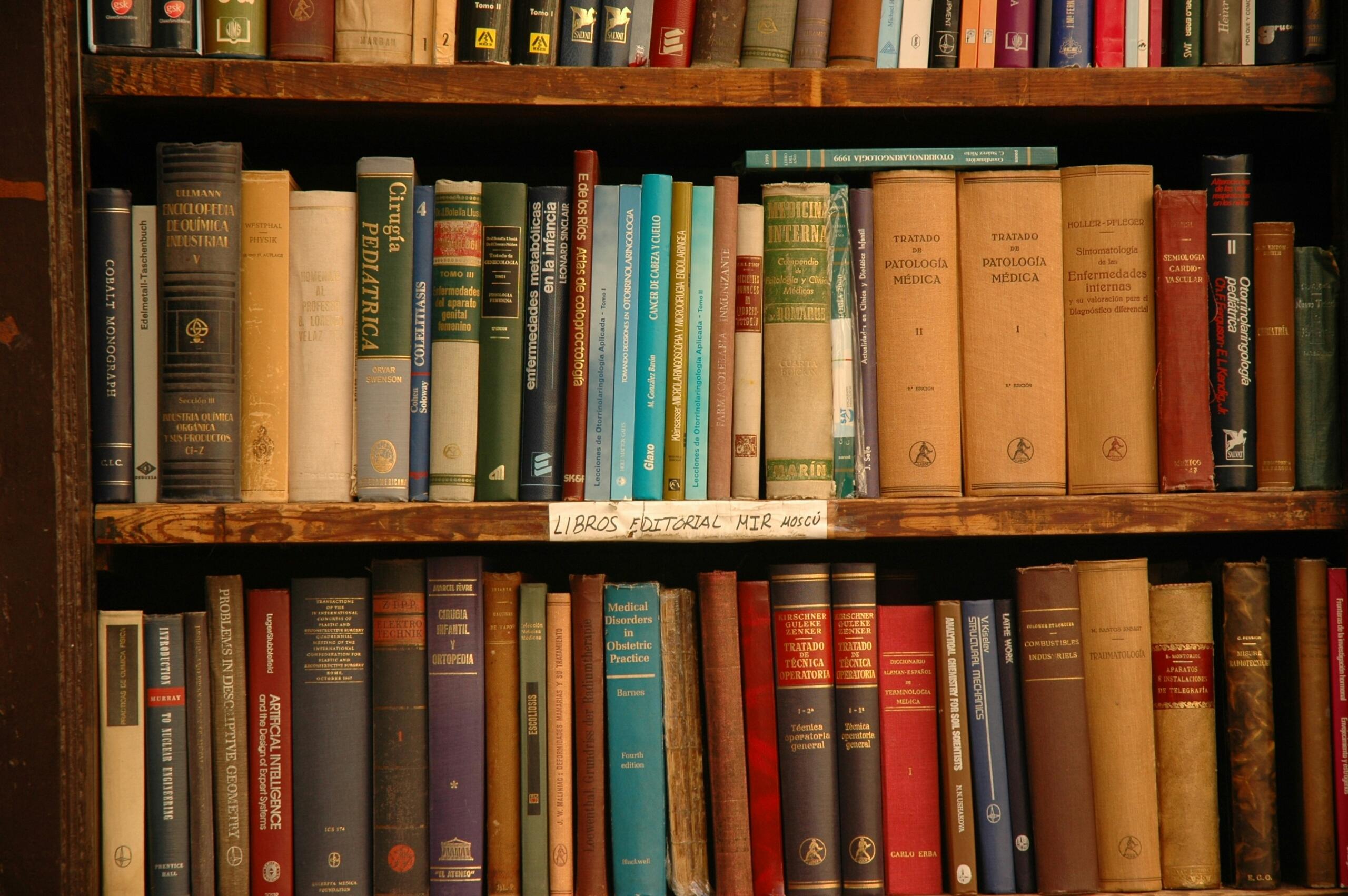 Stare knjige u tvrdom povezu poredane na drvenim policama biblioteke
