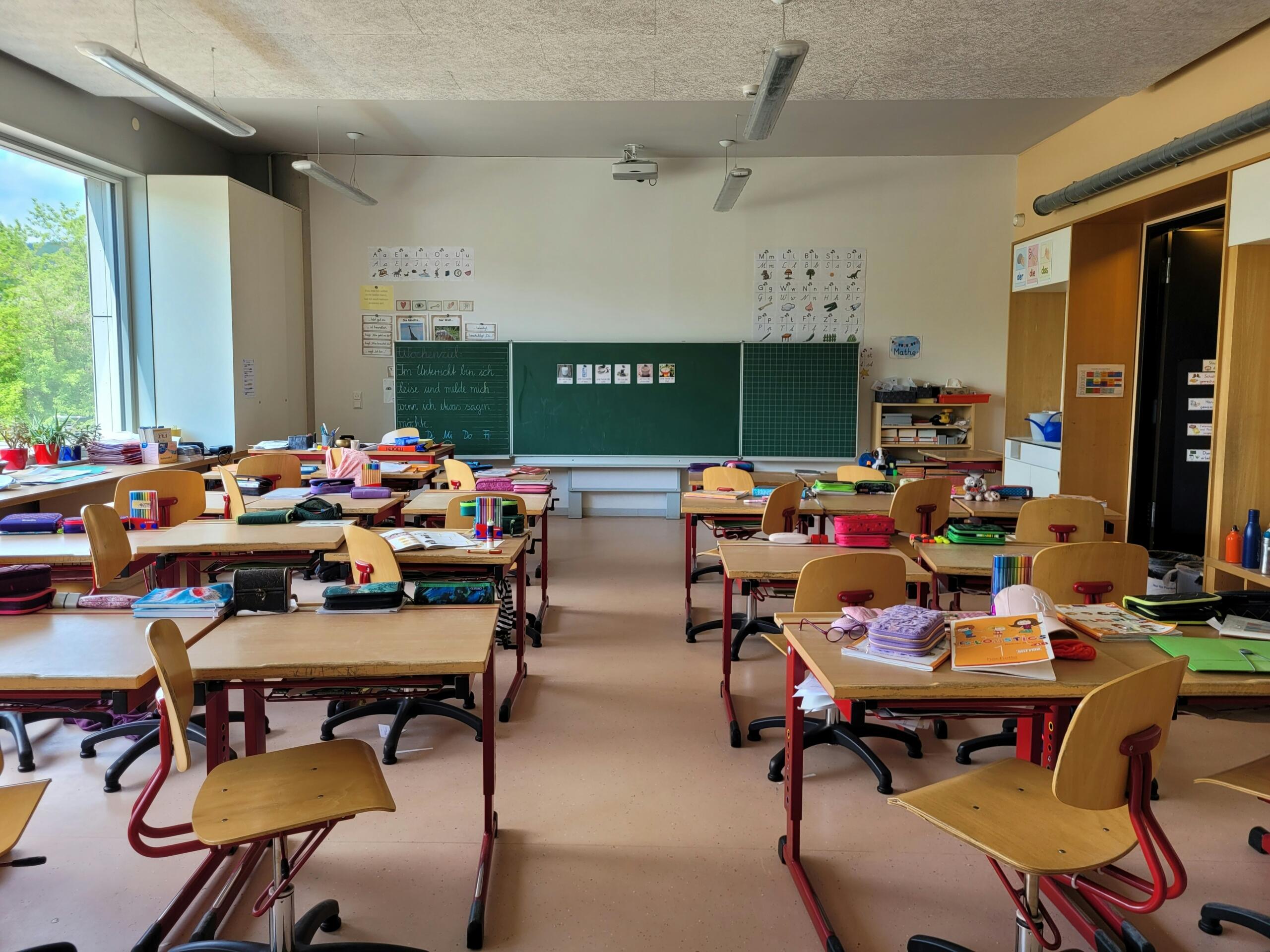 Pogled na prostranu školsku učionicu sa drvenim stolicama, zelenom tablom i priborom na klupama