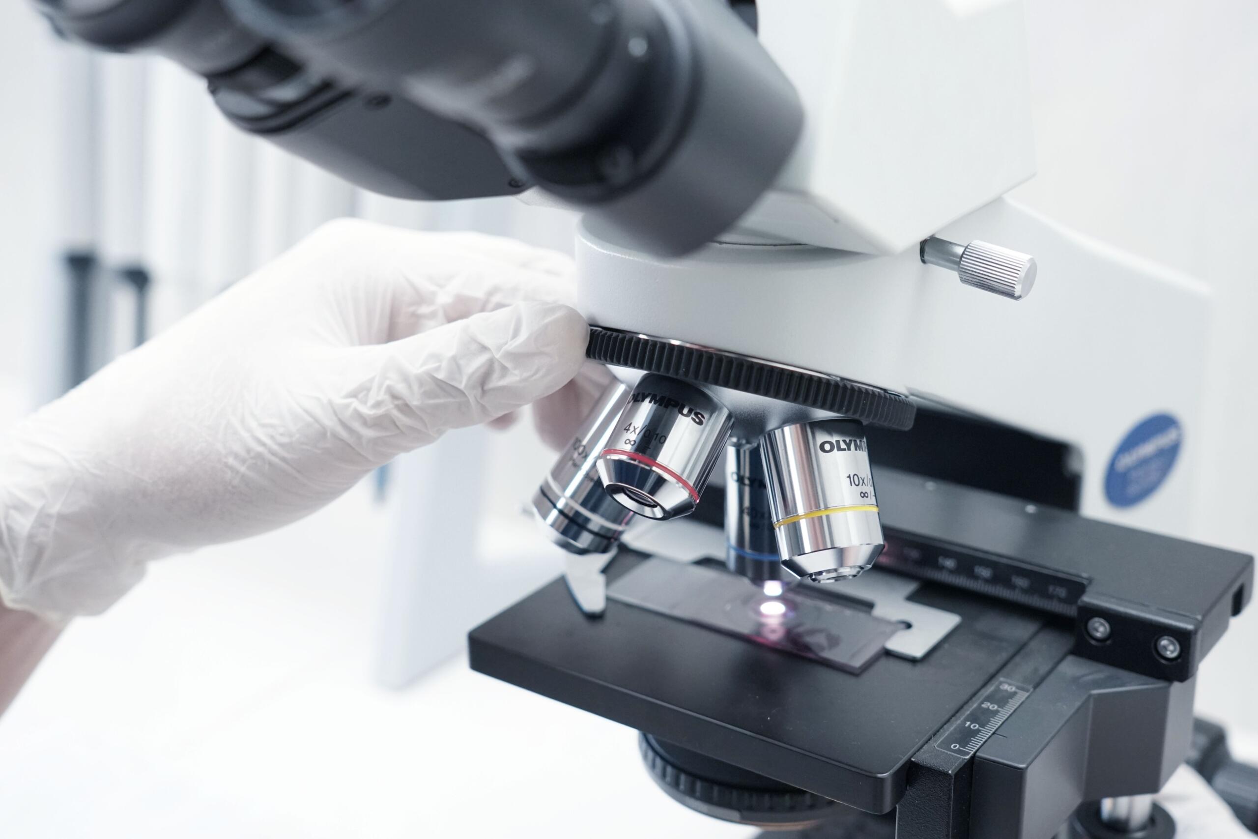 Ruka u bijeloj zaštitnoj rukavici prilagođava objektiv laboratorijskog mikroskopa