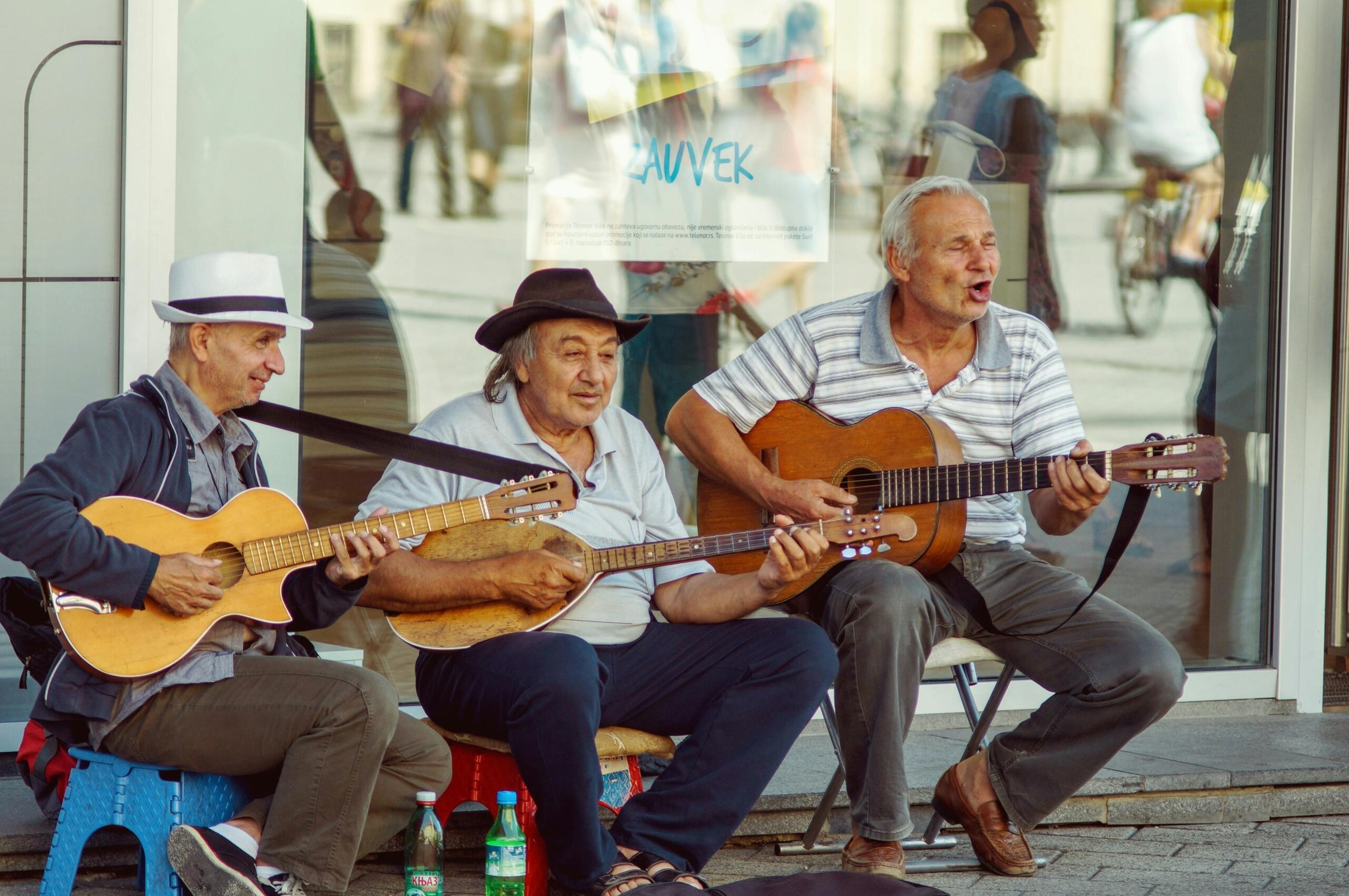 Tri starija ulična muzičara sa akustičnim gitarama i tamburom sviraju i pjevaju na ulici