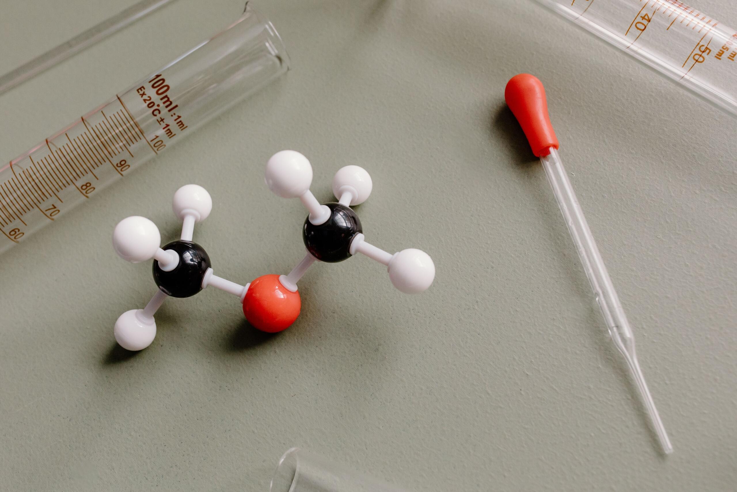 Plastični model hemijske molekule pored staklene pipete i menzure u laboratoriju