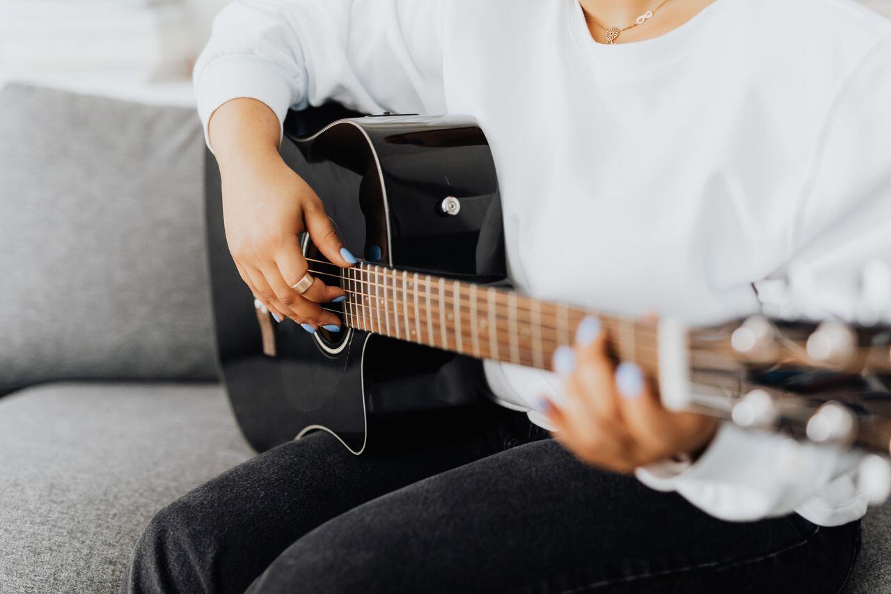 femme assise sur son canape jouant avec sa guitare noire