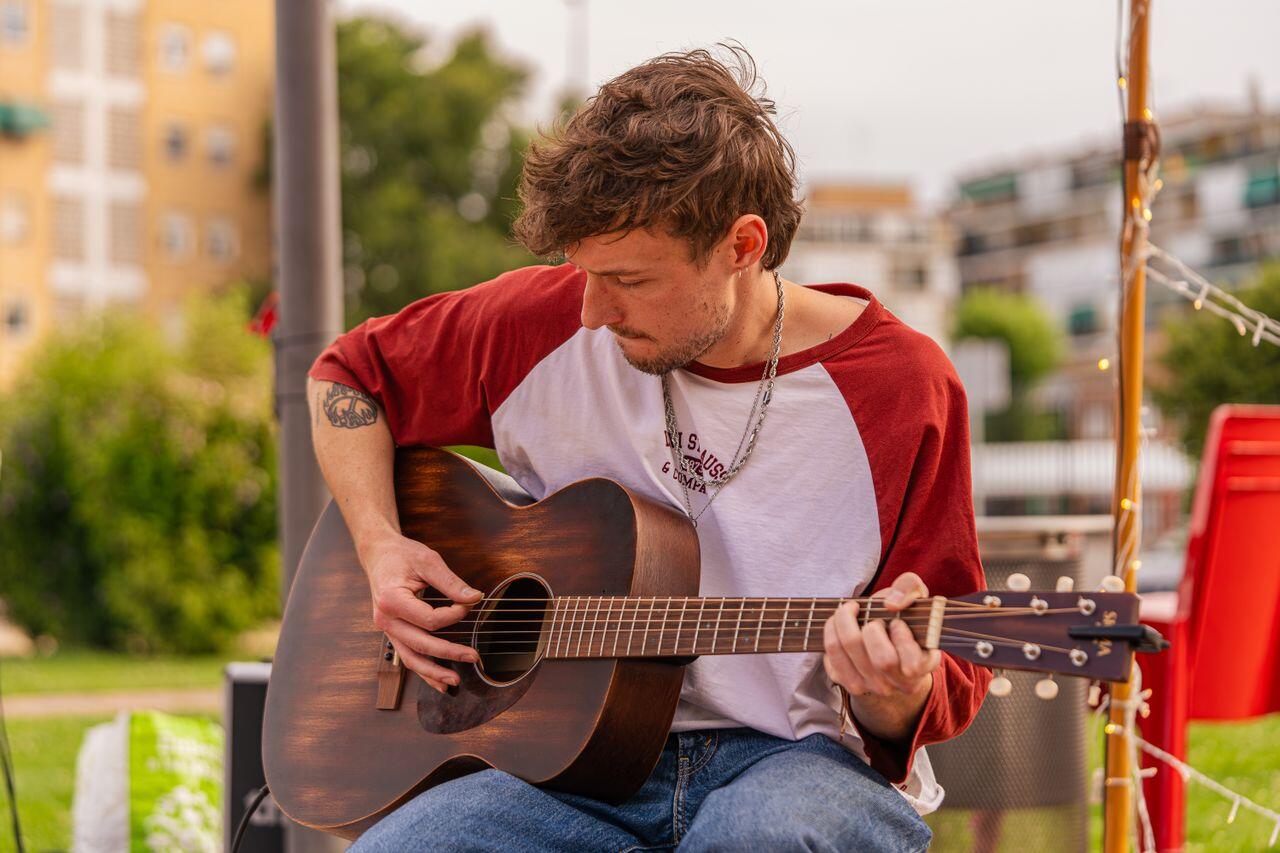 jeune homme en tee shirt rouge et blanc dehors jouant de la guitare