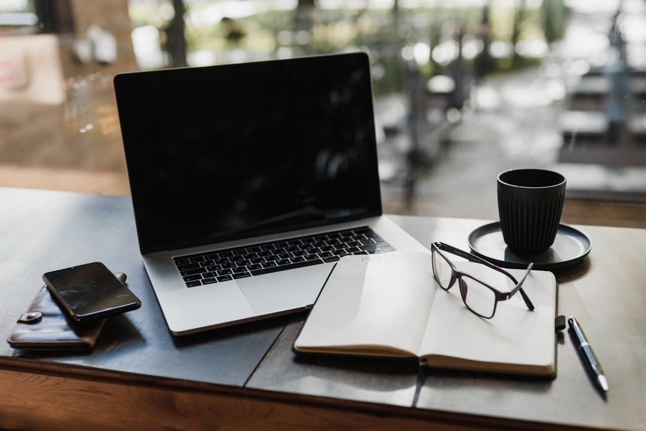 ordi, lunettes, carnet et tasse poses sur une table face a une baie vitree