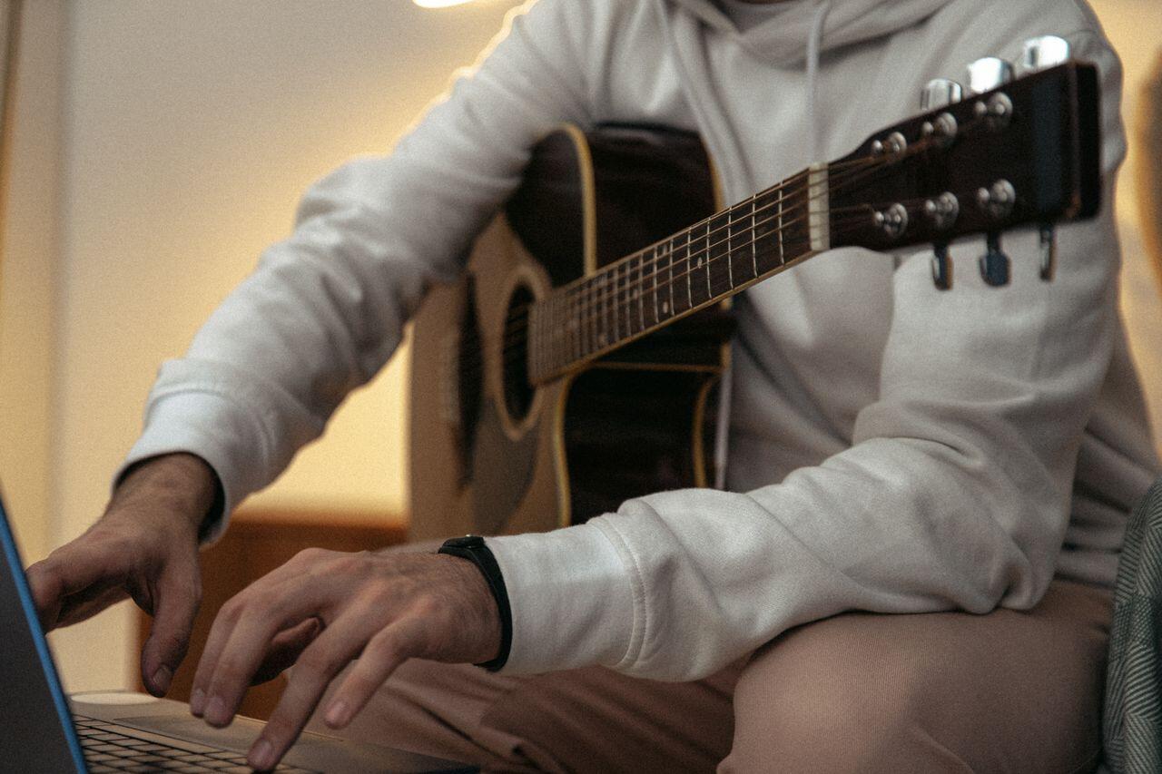 personne avec sweat et une guitare allumant son ordi