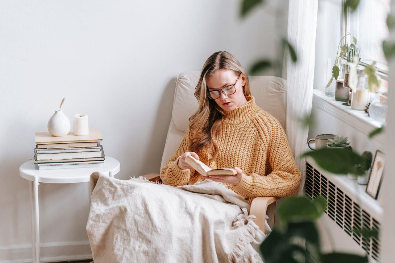 jeune femme lisan un livre sur un fauteuil en pull orange