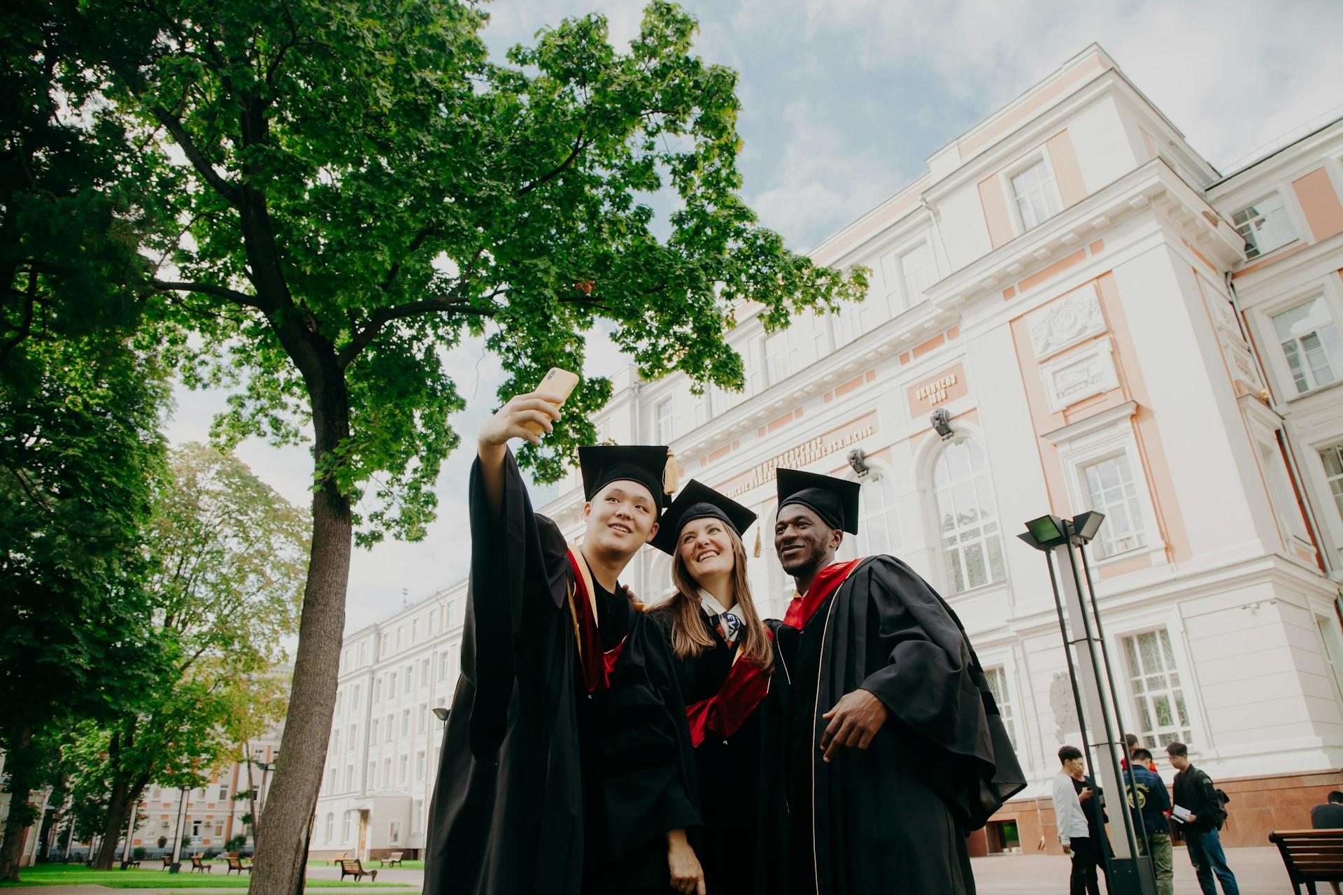trois étudiants diplômés devant une faculté