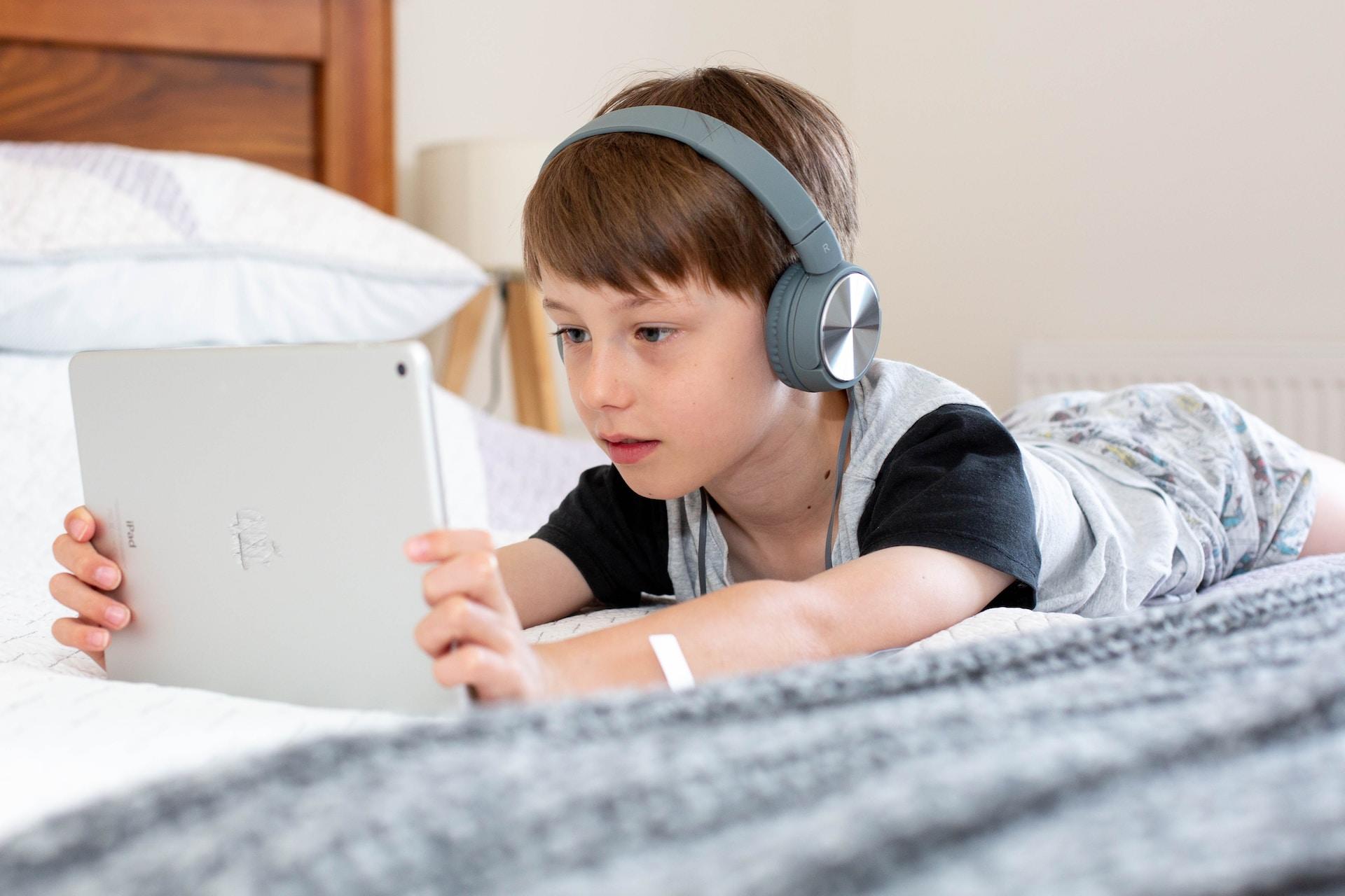 petit garçon sur son lit regardant son ordinateur avec un casque