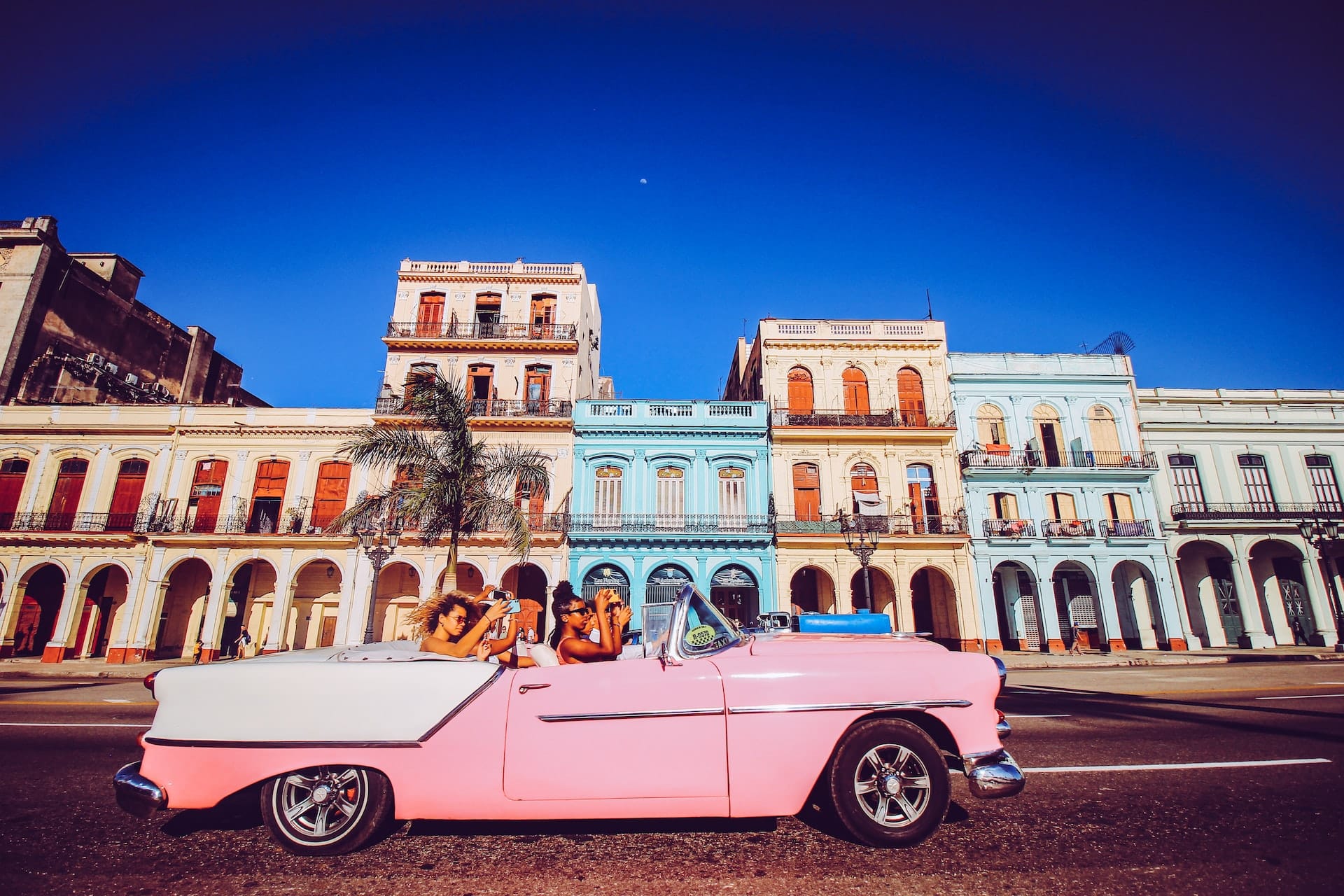 batiments colores de cuba avec une voiture rose remplie de jeunes devant
