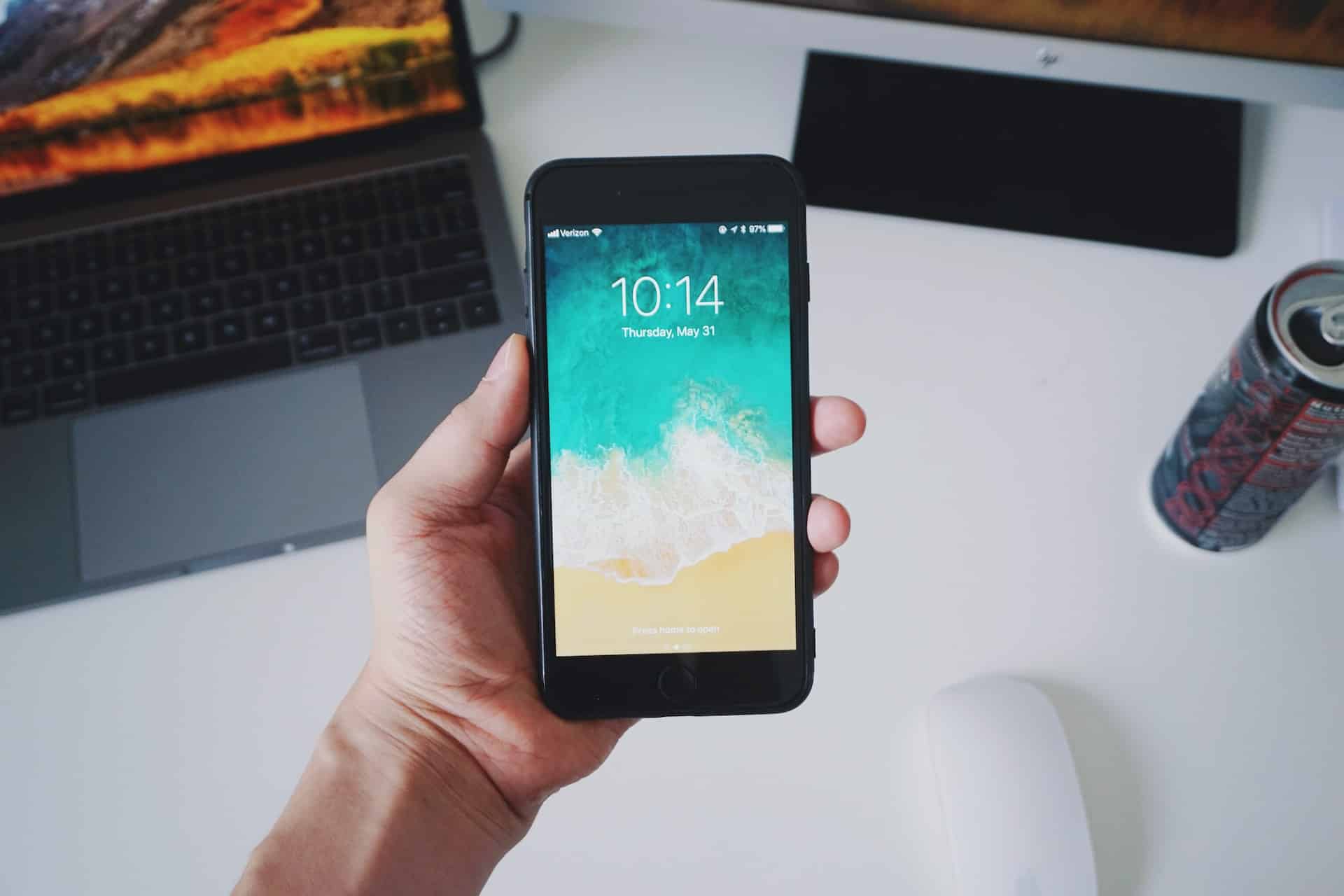 main tenant un smartphone au dessus d une table sur laquelle est posee un laptop