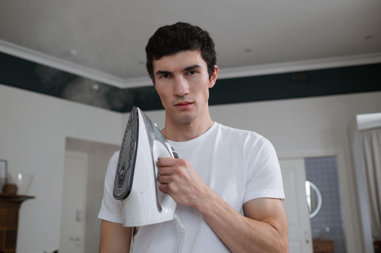 jeune homme en tee shirt blanc prenant la pause avec un fer a repasser
